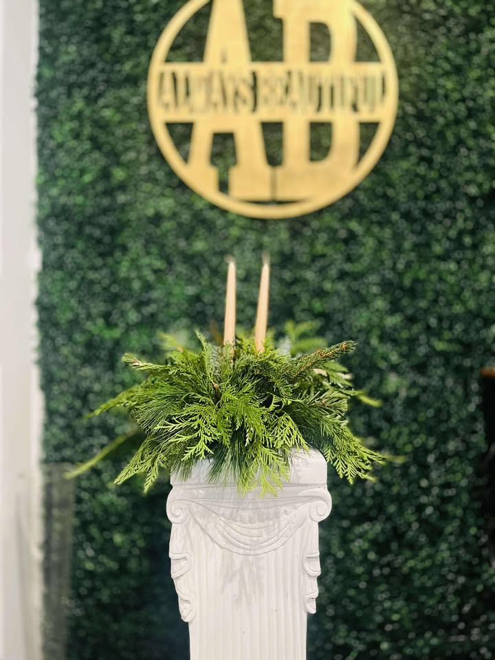 Christmas Centerpiece with Candles - This Christmas centerpiece is a lush and elegant arrangement crafted entirely from vibrant Christmas greens. A rich mix of fragrant evergreen branches, including pine, fir, and spruce, creates a full, textured base, evoking the spirit of a winter forest. Subtle sprigs of cedar lend a soft, feathery texture, while candles nestled within the greens provide a gentle, flickering light, creating a cozy, enchanting atmosphere. This centerpiece brings a peaceful, organic touch to your table, capturing the essence of Christmas with its evergreen beauty and warm candlelight.