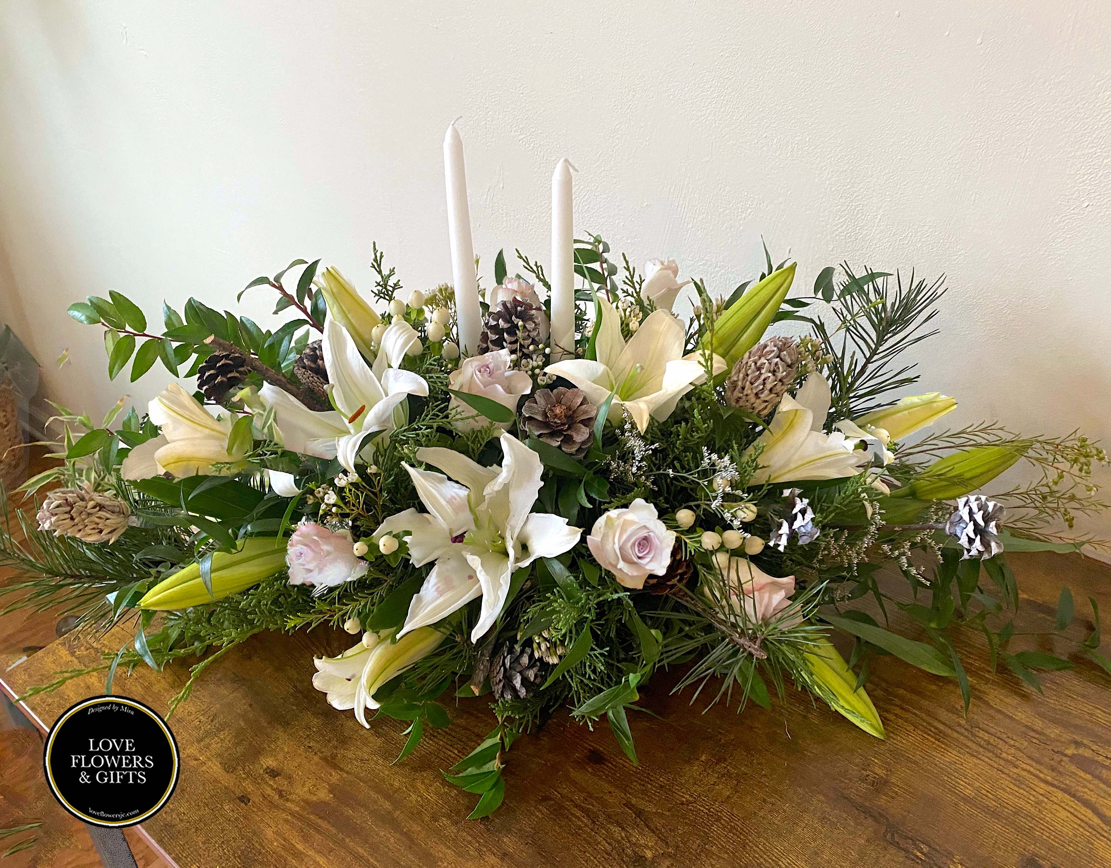 Winter Bless Centerpiece  - Elegant and natural-style long centerpiece, perfect for the Season. Designed with white lilies, silver roses, pinecones, berries in a bed of lush greenery of the center of candles..   Picture Measures 30&quot; by 15&quot;  