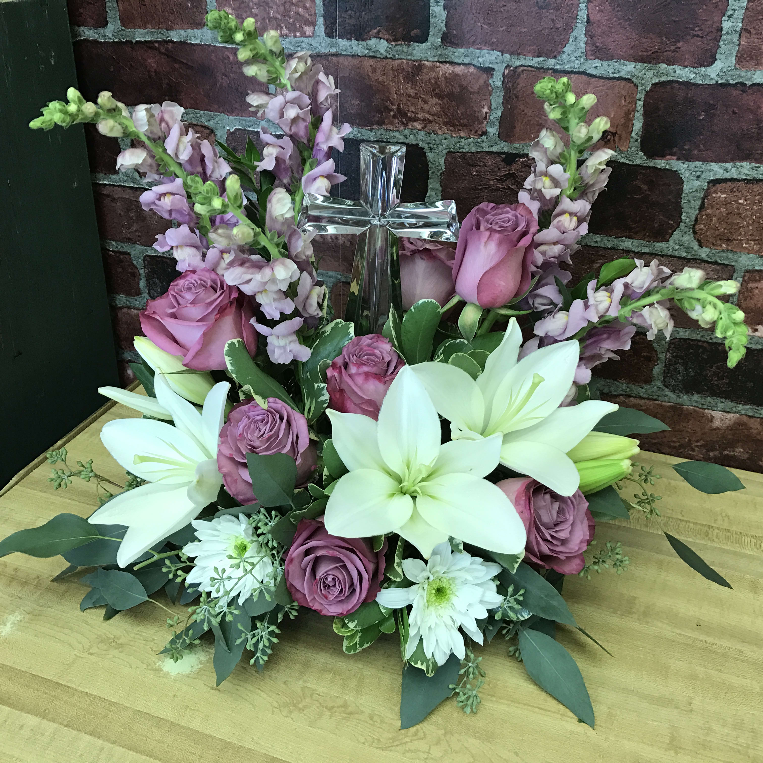 Grace and Majesty Bouquet - The beautiful crystal cross is surrounded by a multitude of gorgeous blooms. Lavender roses, Snapdragons, and White Lilies help bring this bouquet to life. Stunning design perfect for a funeral service or delivered to someone's home. 