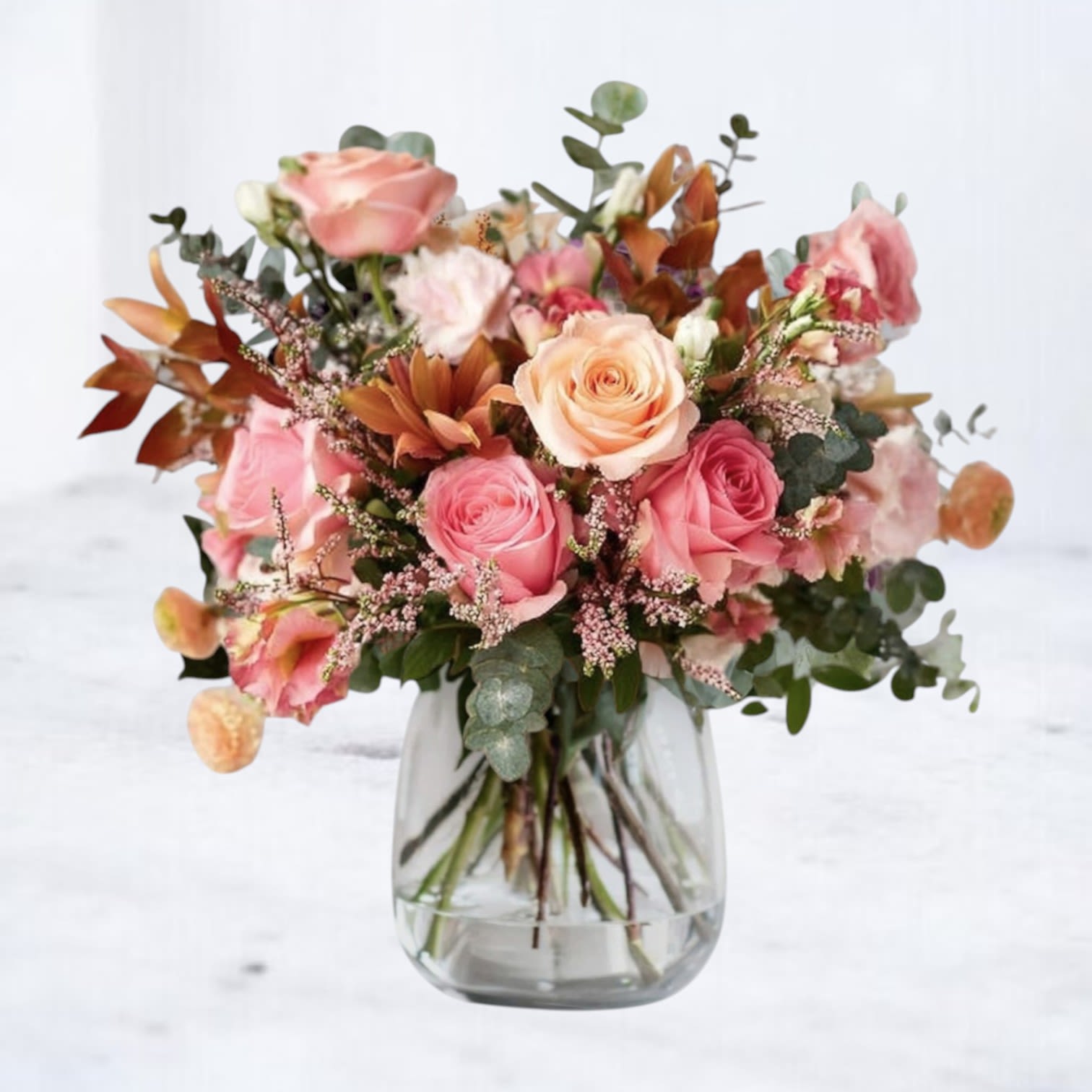 Rosy Dusk Bouquet - The Rosy Dusk Bouquet captures the soft glow of evening with a blend of warm, romantic tones. Peach and blush roses pair with mauve blooms, ivory accents, and airy textural greenery for a look that feels both refined and effortlessly natural. Designed in a modern vase, this arrangement brings a gentle, inviting charm to any occasion—birthdays, thank-yous, anniversaries, or simply because.  Thoughtfully composed with our signature attention to detail, Rosy Dusk adds a touch of warmth and beauty to any room. Available for same-day flower delivery in Houston and surrounding areas.  Substitution Disclaimer: Due to seasonal availability, some blooms may be replaced with similar varieties of equal or greater value to maintain the design’s look and character.