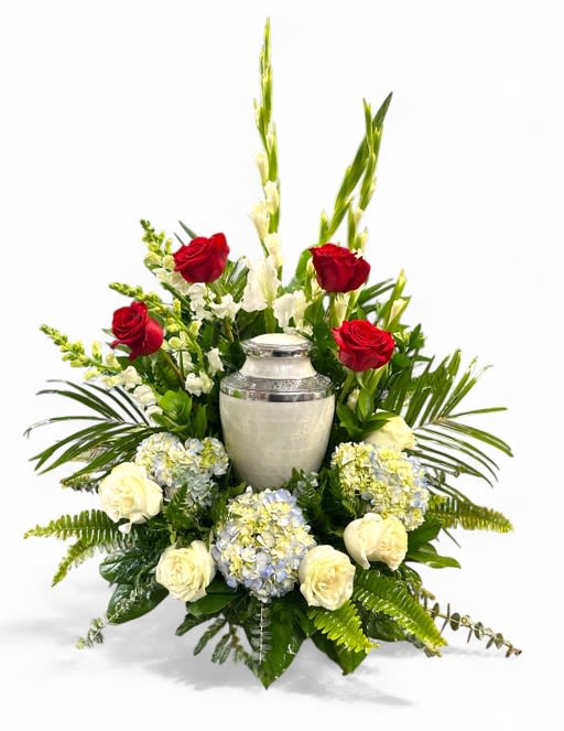 Freedom's Valor Urn Patriotic Tribute - The Freedom's Valor Urn Surround is a breathtaking tribute that beautifully embodies patriotism and honor. Crafted with a harmonious blend of vibrant and elegant blooms, this surround features tall white gladiolas and delicate white snapdragons, symbolizing purity and remembrance. Surrounding these are lush blue hydrangeas, adding fullness and softness to the arrangement. Accentuating the design are striking red and white roses, representing sacrifice and unity, while the mixed green foliage and eucalyptus provide a rich, natural backdrop, enhancing the overall patriotic theme. This stunning arrangement serves as a heartfelt tribute to honor and valor, celebrating the spirit of freedom with dignity and grace.  (Urn or Photo not included.)
