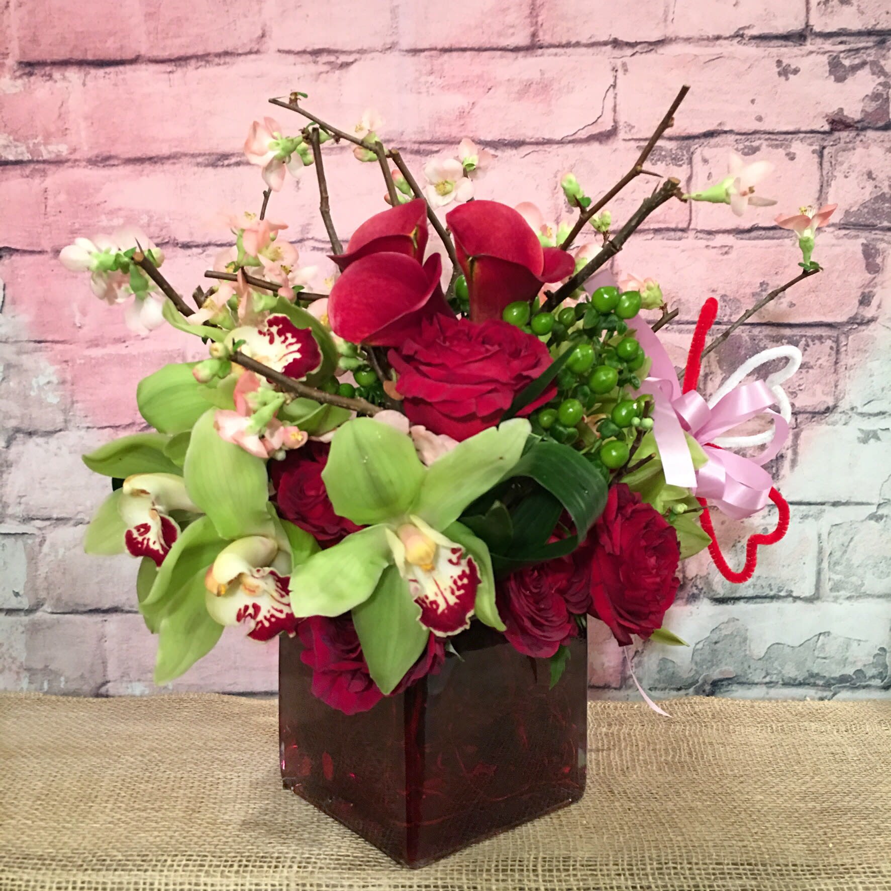 XOXO - ASSORTMENT OF DEEP RED ROSES, RED CALLA LILIES, GREEN HYPERICUM, GREEN CYMBIDIUM ORCHID, AND QUINCE BRANCHES. 