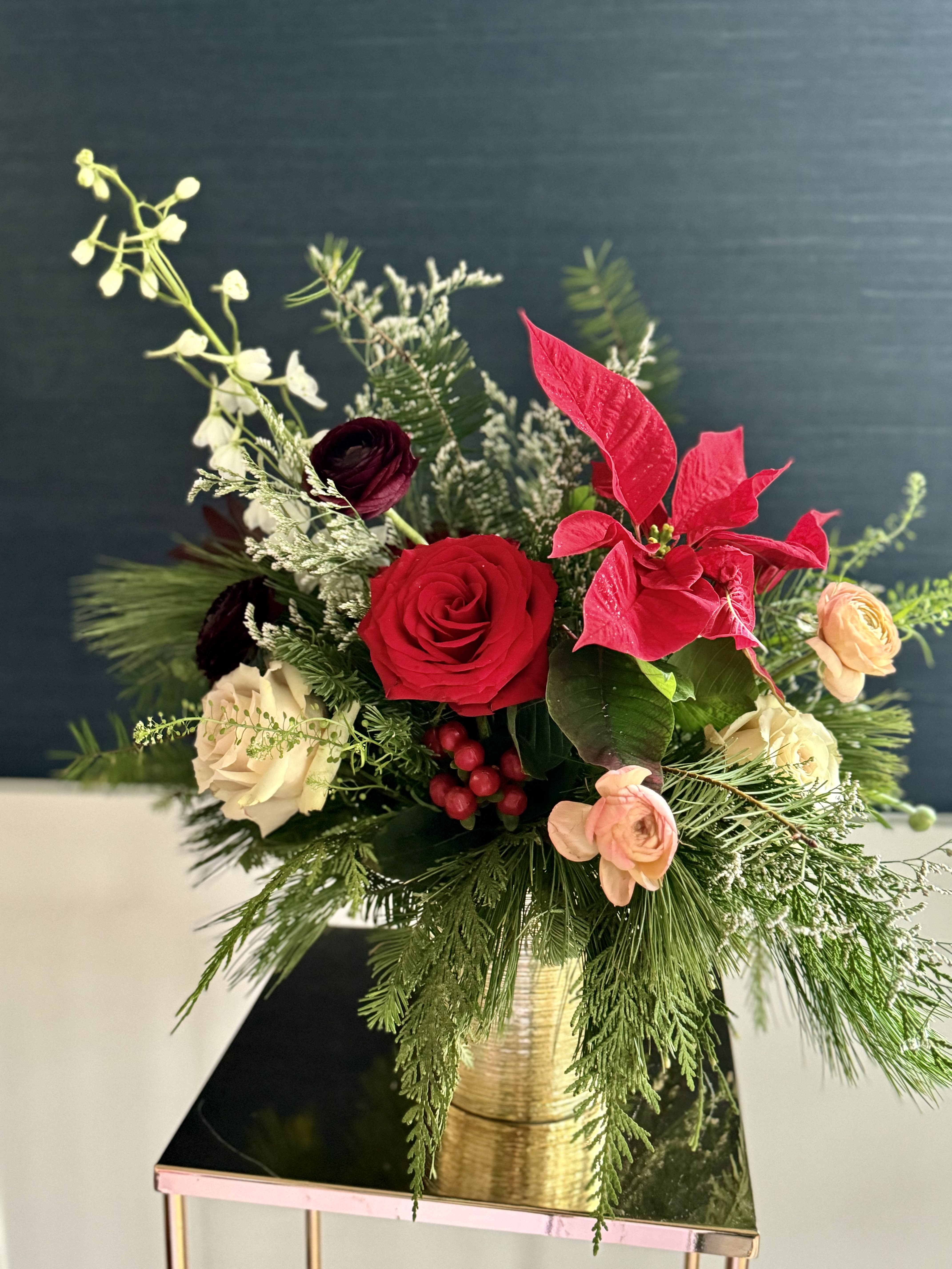 Be Jolly - A festive holiday arrangement with winter greens in a gold vase. Medium height.