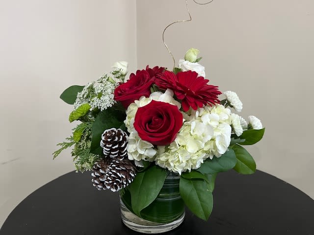Christmas Vase Centerpiece - Elegant arrangement made up of red roses, red gerber daisies, white hydrangea, white lisianthus, fillers flowers and mixed holiday greens with decorative ornaments.