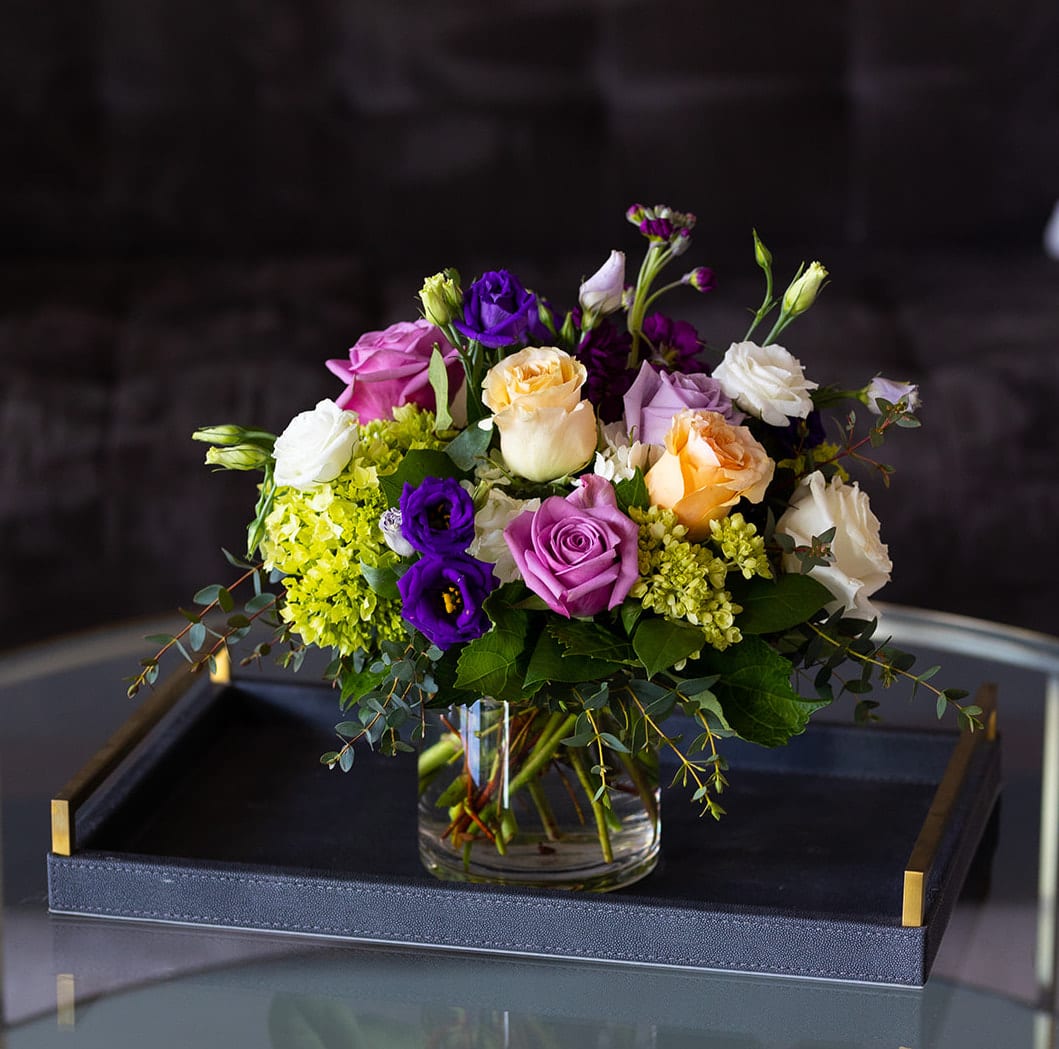 A Day in Paris - Market Size  - A best seller! Vibrant and inspiring blooms that remind us of a day in the city of love -- Paris! Garden roses, standard roses, Hydrangea, and Lisianthus in spring shades of white, green, peach, lavender and purple. Who wouldn't want to receive a day in Paris from someone who care about them?   Our market collection features fresh cut flowers in a clear glass vase. We created this size to send for birthdays, a pick-me-up, a thank you or to also work as a centerpiece for parties and events. These designs are made in a 5” clear glass cylinder vase.   Product Details: This arrangement is approximately 10” tall and 8” wide.