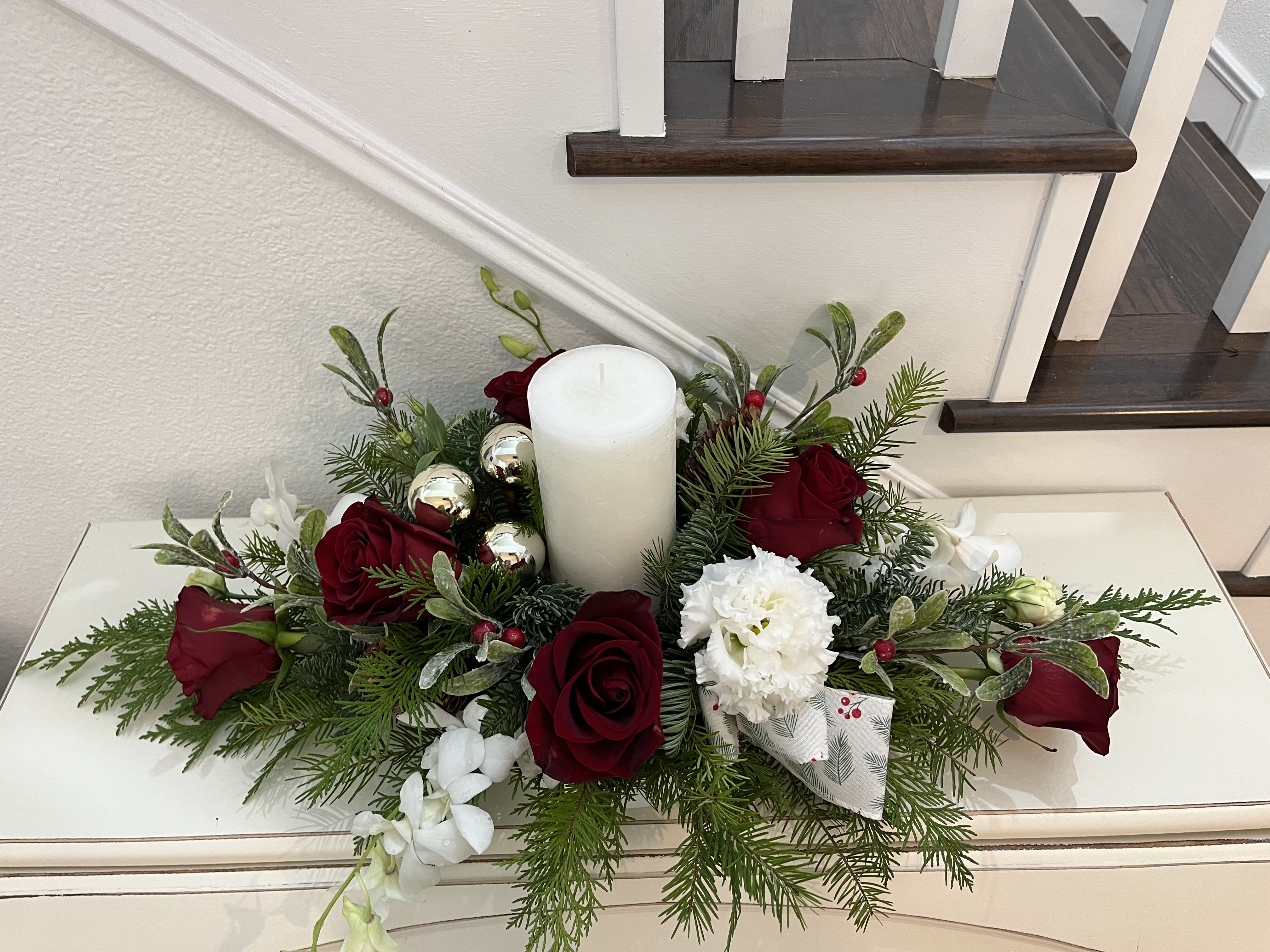 Christmas rose centerpiece  - Candle arrangement with Christmas greens, roses, lisianthus  , dendrobium orchids, gold bulbs, and ribbon