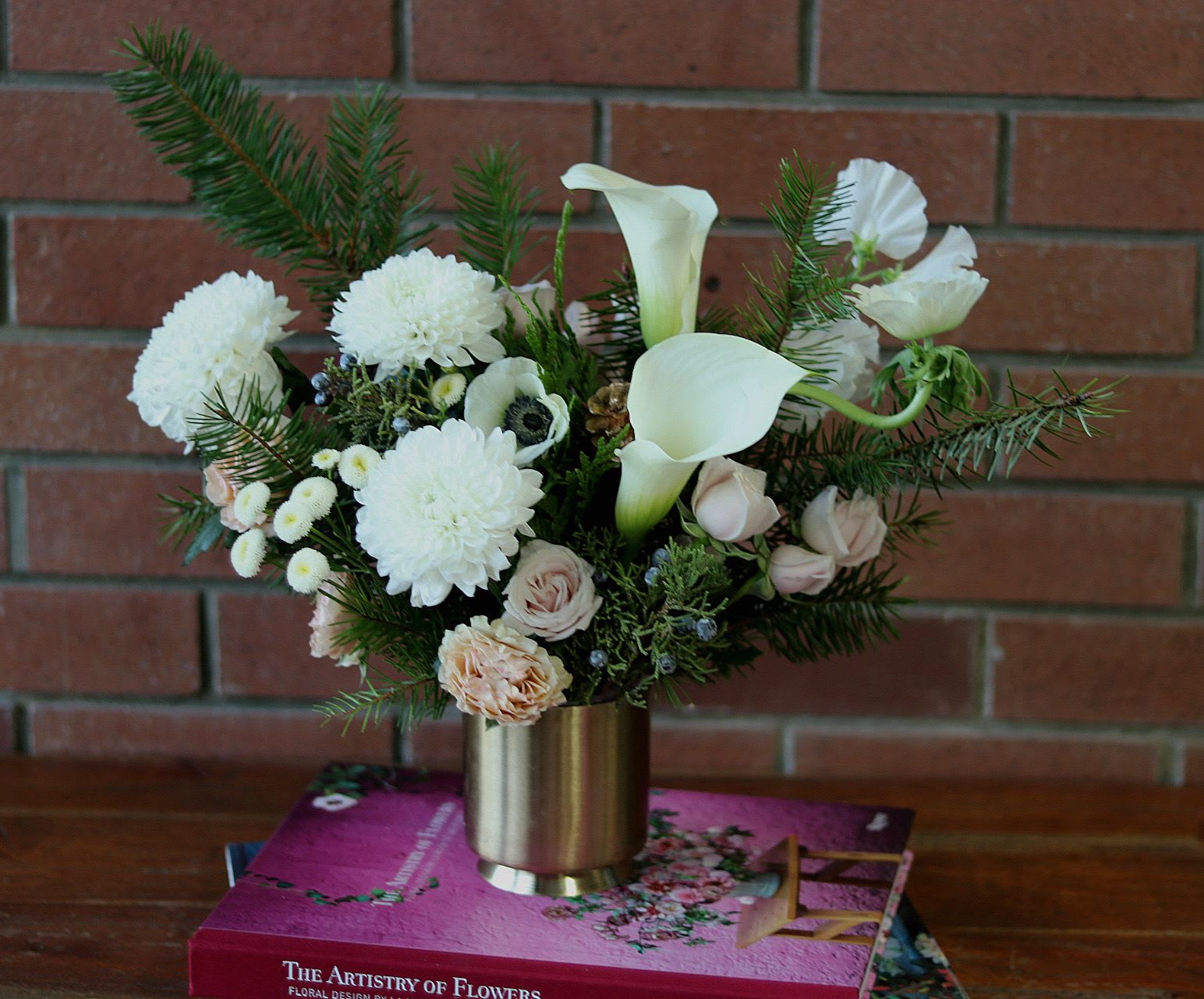 Elegant Winter Bouquet  - Elegant Winter Bouquet: Two size options: Standard as Pictured or Premium in the same gold container a large version with added extra flowers to value.  Experience the charm of winter with the Elegant Winter Bouquet, a stunning creation by Venetian Flowers. Housed in a chic gold modern container, this exquisite arrangement features a harmonious blend of seasonal evergreens that evoke the essence of a serene winter landscape.   Delicate white anemones and sleek white mini calla lilies add a touch of sophistication, while blush spray roses introduce a soft warmth to the composition. The vibrant ball mums provide a playful contrast, completing this bouquet with a pop of texture and color.   Perfect for holiday celebrations, elegant gatherings, or as a luxurious gift, the Elegant Winter Bouquet embodies the beauty and grace of the season, making it a must-have centerpiece for any winter occasion.