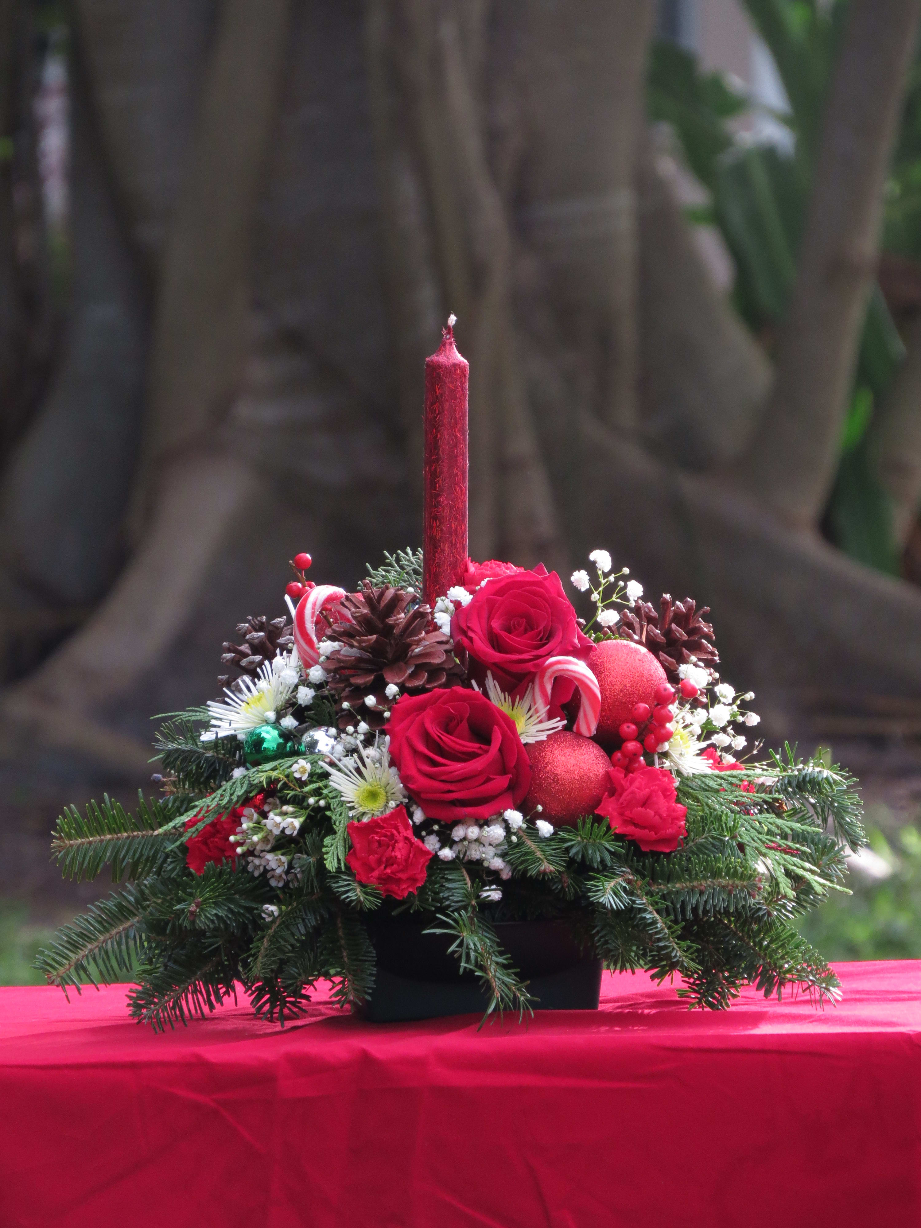 Lasting Traditions Centerpiece  - Red roses, red carnations and mini carnations, mixed evergreens, pine cones, ilex berries and more with a designer red candle. Deluxe: extra flowers Premium: extra flowers 2 designer candles instead of 1