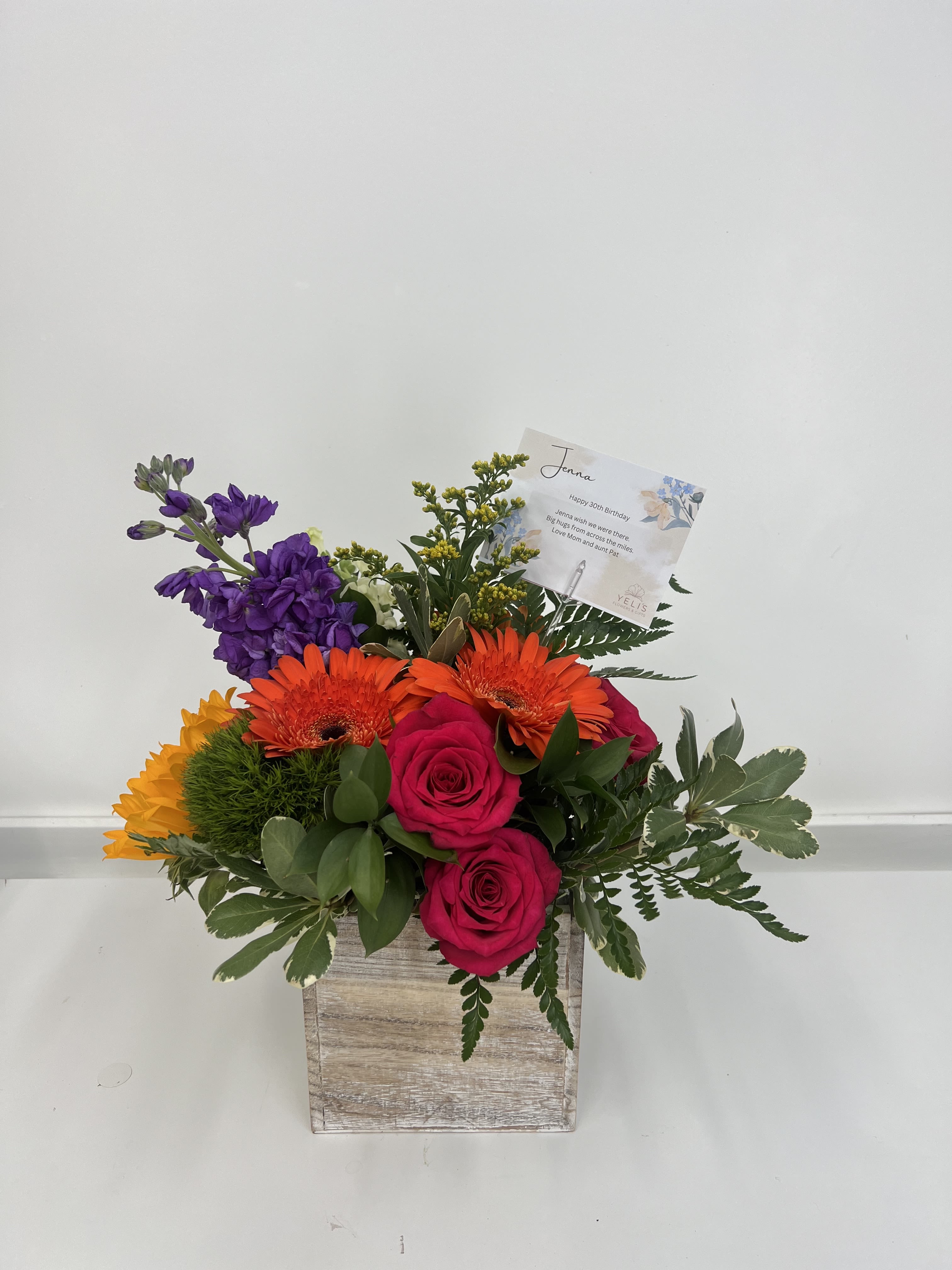 Vibrant Colors in Box  - This vibrant arrangement features cheerful sunflowers, bold gerberas, fragrant stock, and classic roses, all beautifully arranged in a rustic wooden square box. The bright, sun-kissed blooms create a joyful and warm display, while the wooden box adds a touch of natural charm. Perfect for bringing warmth and happiness to any space, this arrangement is ideal for celebrating special occasions or brightening someone's day with its radiant colors and fresh, uplifting style.