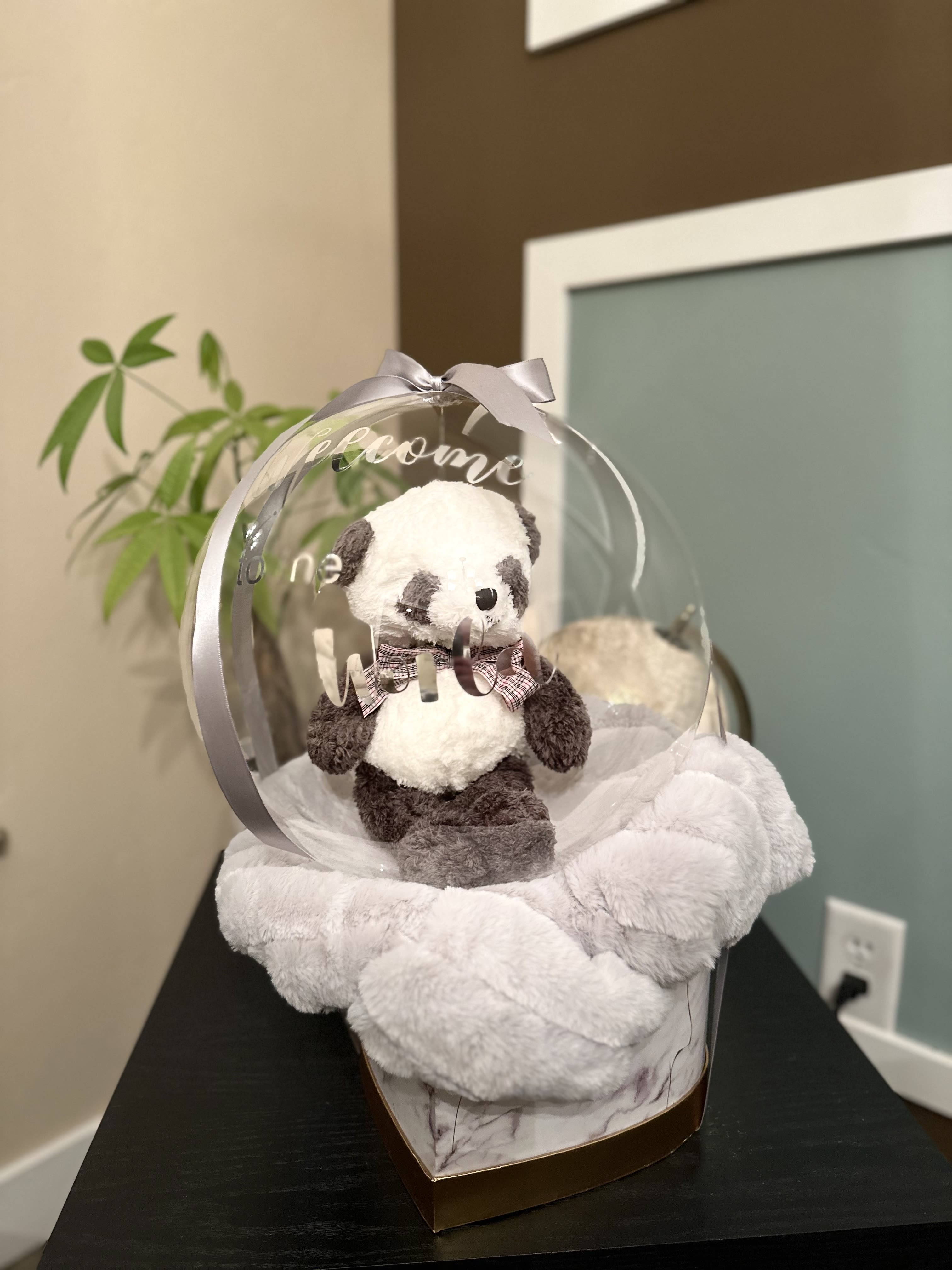 Welcome to the Worl Baby  - This delightful new baby gift features a charming plush bear nestled inside a clear bubble balloon, creating a whimsical and enchanting display. Accompanying the balloon is a soft, cozy blanket, perfect for cuddling. The blanket's color may vary, adding a unique and personalized touch to each gift. Ideal for welcoming a new baby, this thoughtful present combines warmth, comfort, and playful charm.