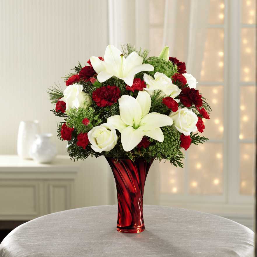 Holiday Celebrations Bouquet - This fresh and contemporary bouquet includes Christmas red carnations, snowy white lilies and roses, and lovely Queen Anne's lace all beautifully punctuated with Christmas greens. Makes a thoughtful, memorable way to say, &quot;Merry Christmas!&quot;