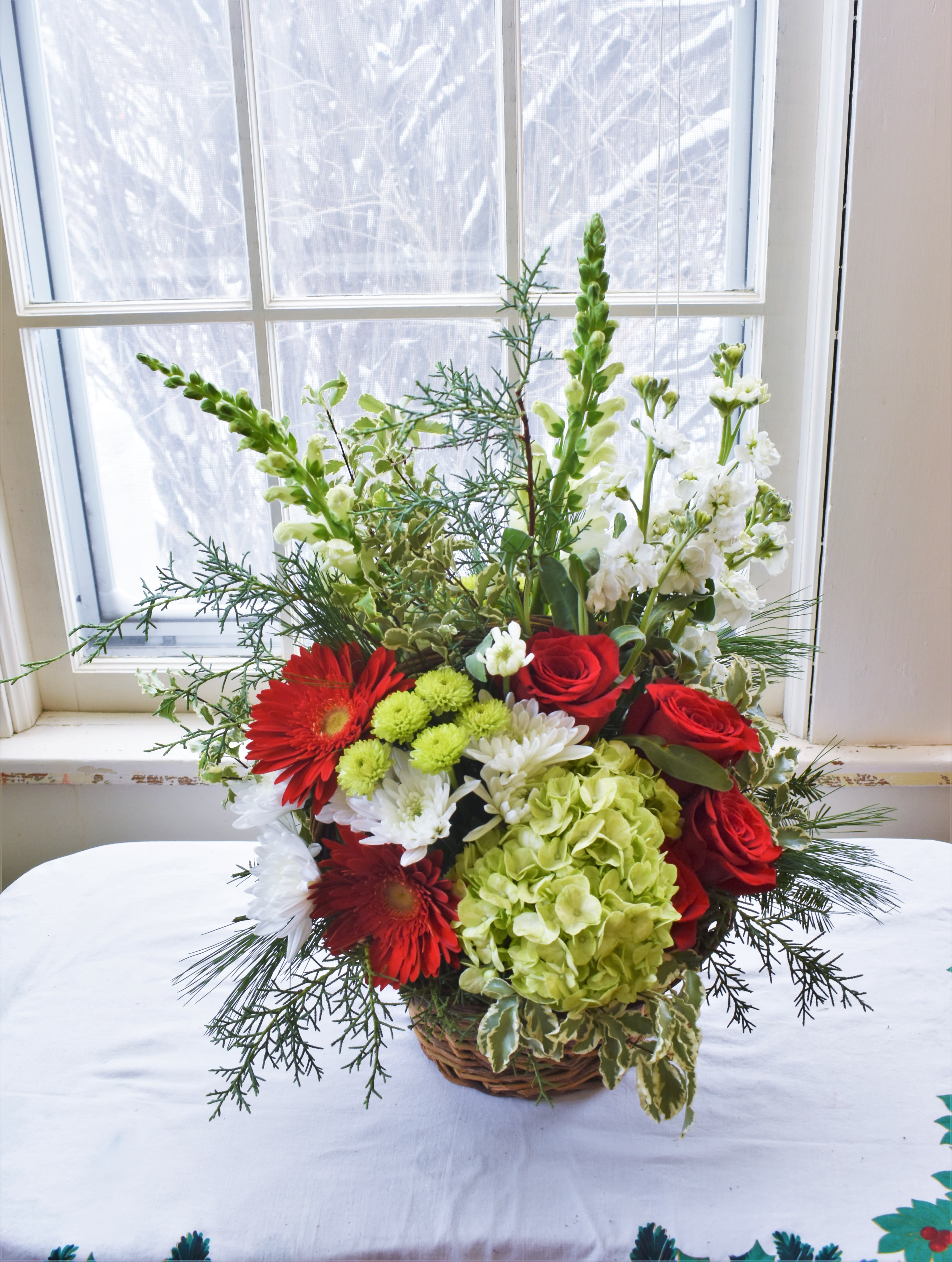 Tidings of Joy - A festive bouquet of green, white, and red! Red gerber diaises, roses, green hydrangea, button mums, and white mums, and snapdragons are designed in a basket and accented with winter pine. The perfect gift for the season! 