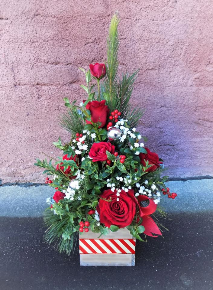 Oh Christmas Tree - A perfect gift for any occasion! This cheery tree-shaped seasonal arrangement is designed with long-lasting boxwood and assorted winter greens.  Crimson roses and soft babysbreath accent throughout, as well as shiny Christmas ornaments. Truly a festive and classic arrangement! 