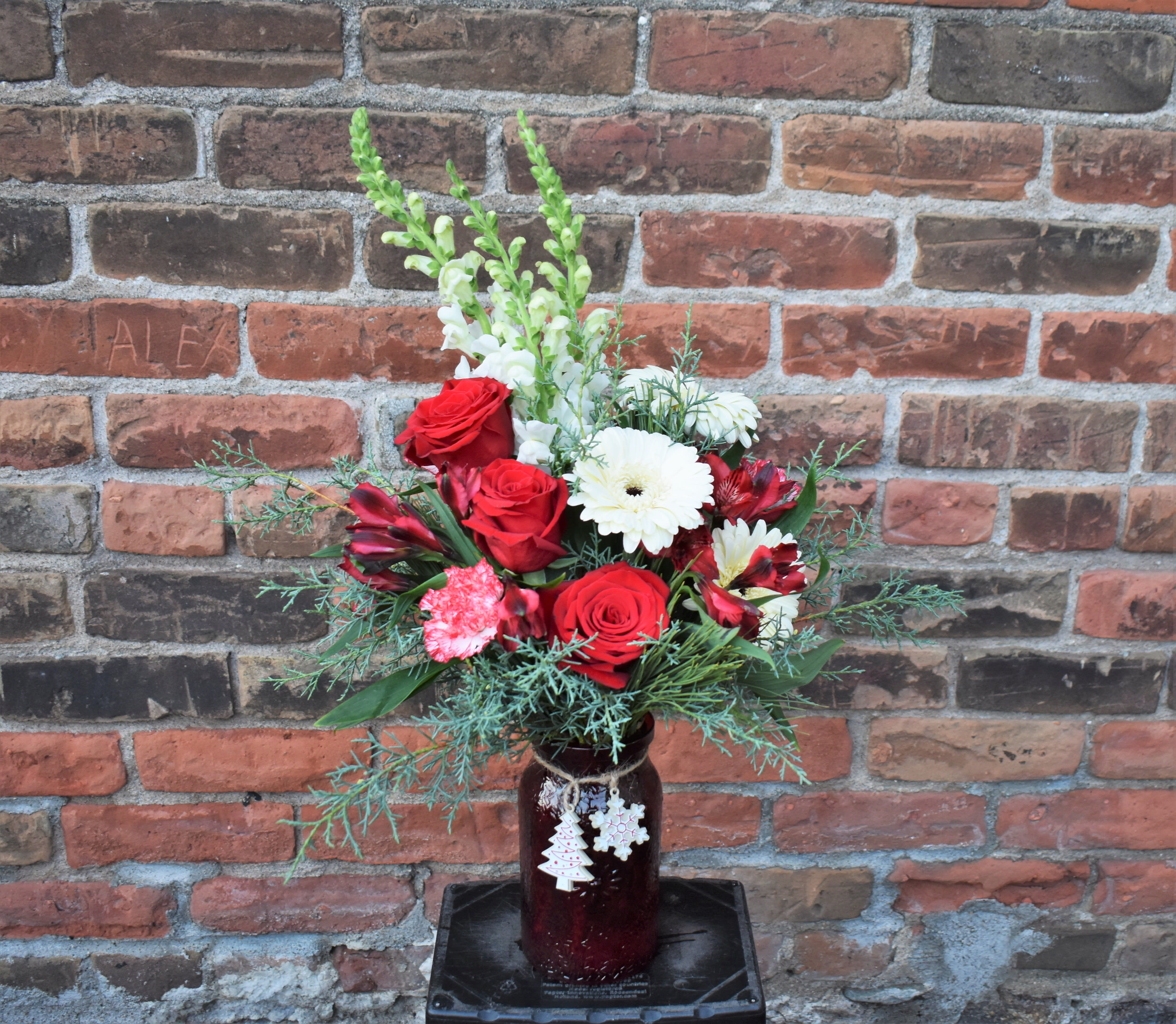 Christmas Cookie - Fresh pine, red roses, peppermint carnations, red alstormeria, white Gerbera daisies, and white snapdragons are designed in a red vase and accented by small ceramic cookie ornaments...a fun and nostalgic way to celebrate the Holidays! 