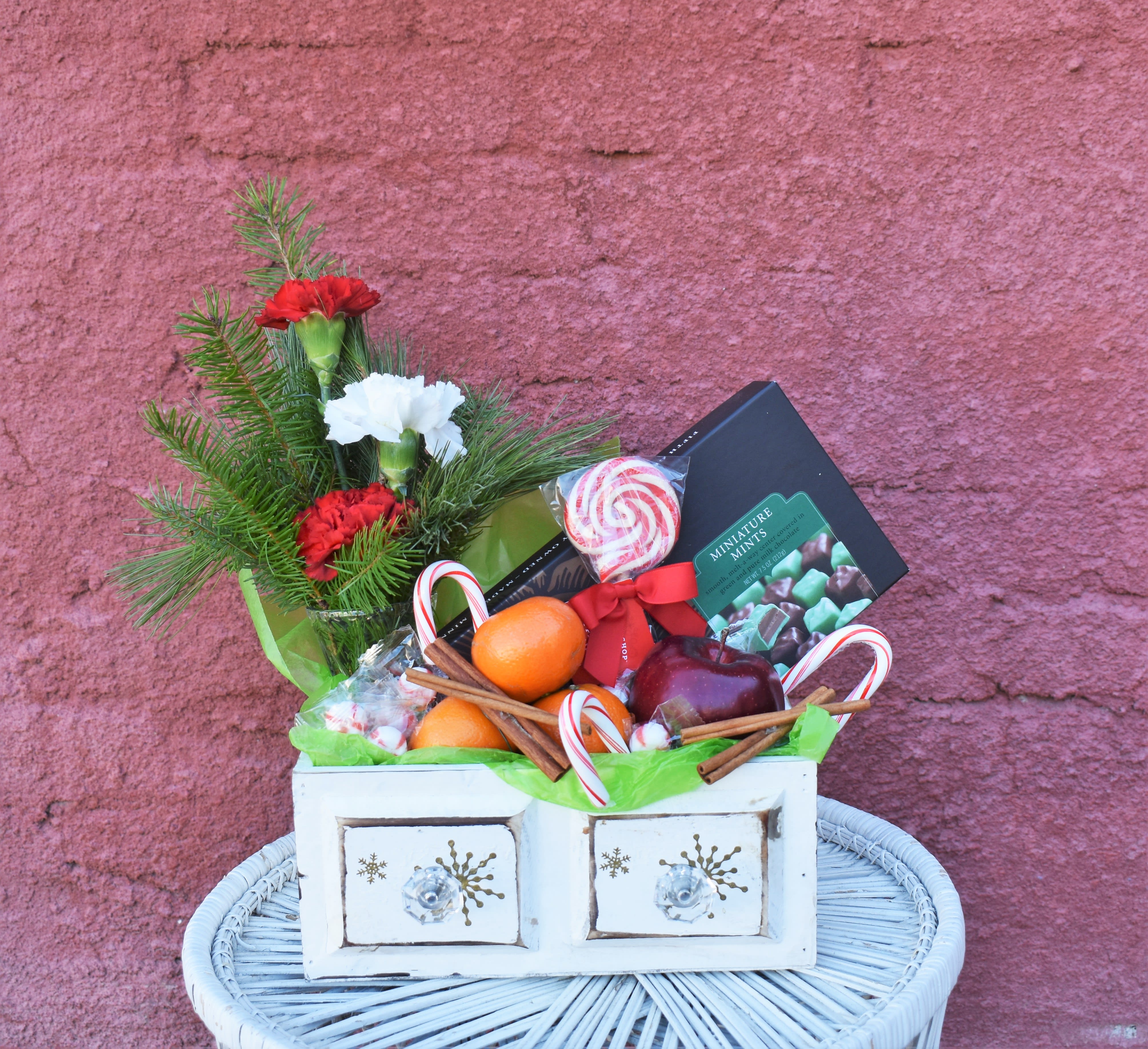 Visions of Sugarplums - A fun and colorful assortment of fruit, flowers, and chocolates are arrangement in a white drawer container and accented with peppermints.  Designs include apples, clementines, made-in-MN Abdallah mint chocolates, carnation vase design, and peppermint candies...the perfect gift to celebrate the season! 