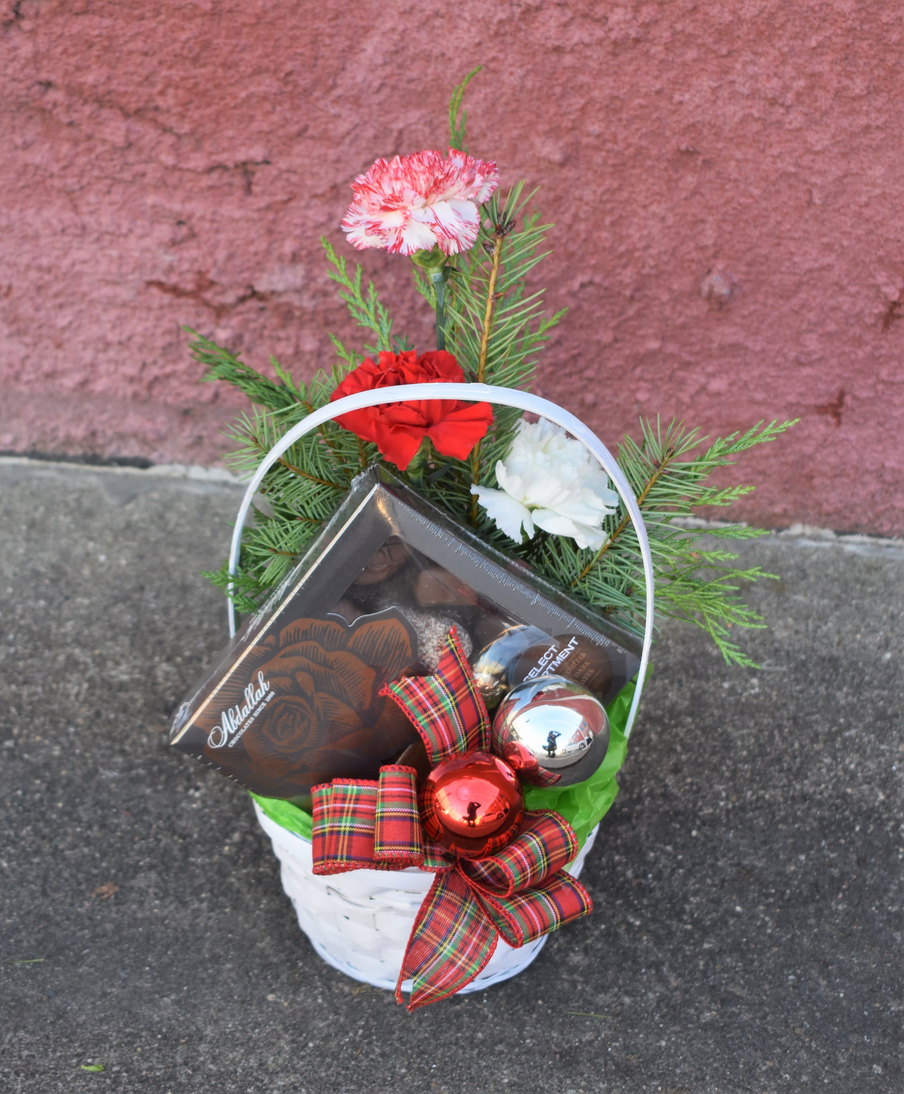 Santa's Helper - Looking for a cute Christmas gift? A small vase arrangement of carnations and pine are nestled in a white-washed wicker basket with made-in-MN chocolates and accented with Christmas bows and ornaments! A fun way to send a thoughtful gift this season! 