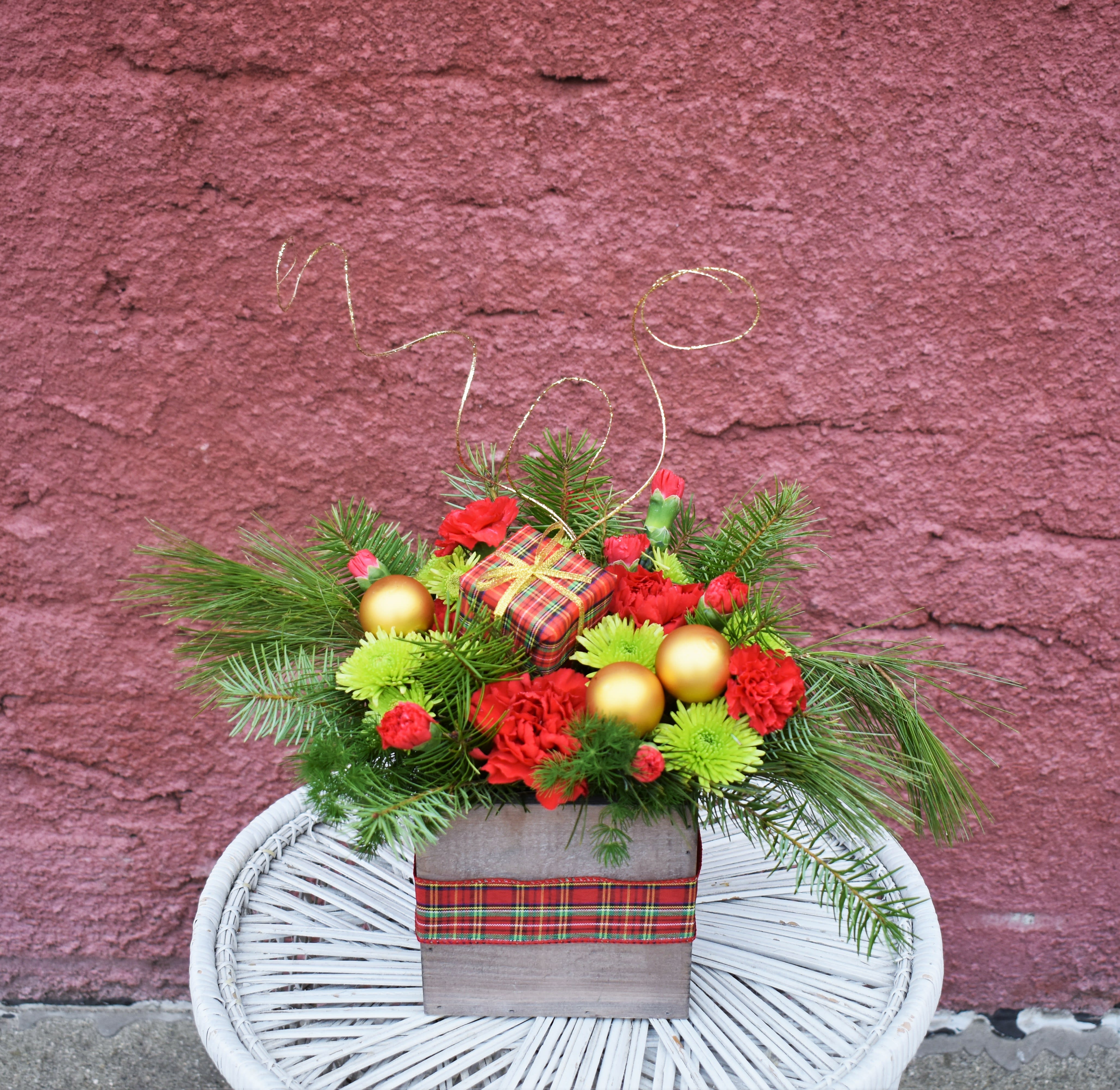Christmas Present  - Looking for a perfect Christmas present? This fun bouquet is full of fresh pine, red carnations, and bright green button mums. Designed in a wooden cube and adorned with a plaid present, bow, and gold ornaments, it is a fun and colorful way to celebrate the season! 