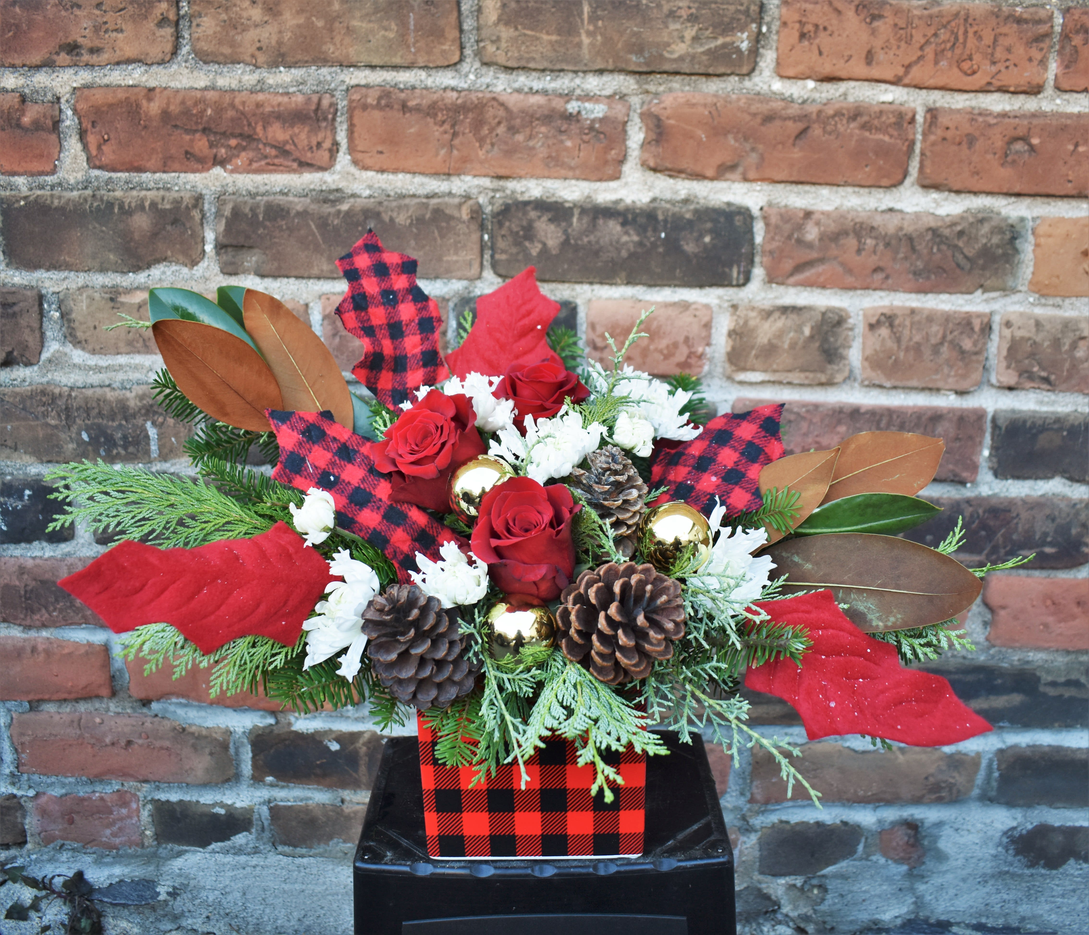 Buffalo Gal - Who loves Buffalo plaid?!  Fresh pine, white mums, red roses, magnolia, pinecones, and gold ornaments are designed in a fun buffalo plaid ceramic vase and accented by buffalo plaid fabric leaves...a super fun and rustic way to celebrate the season! 