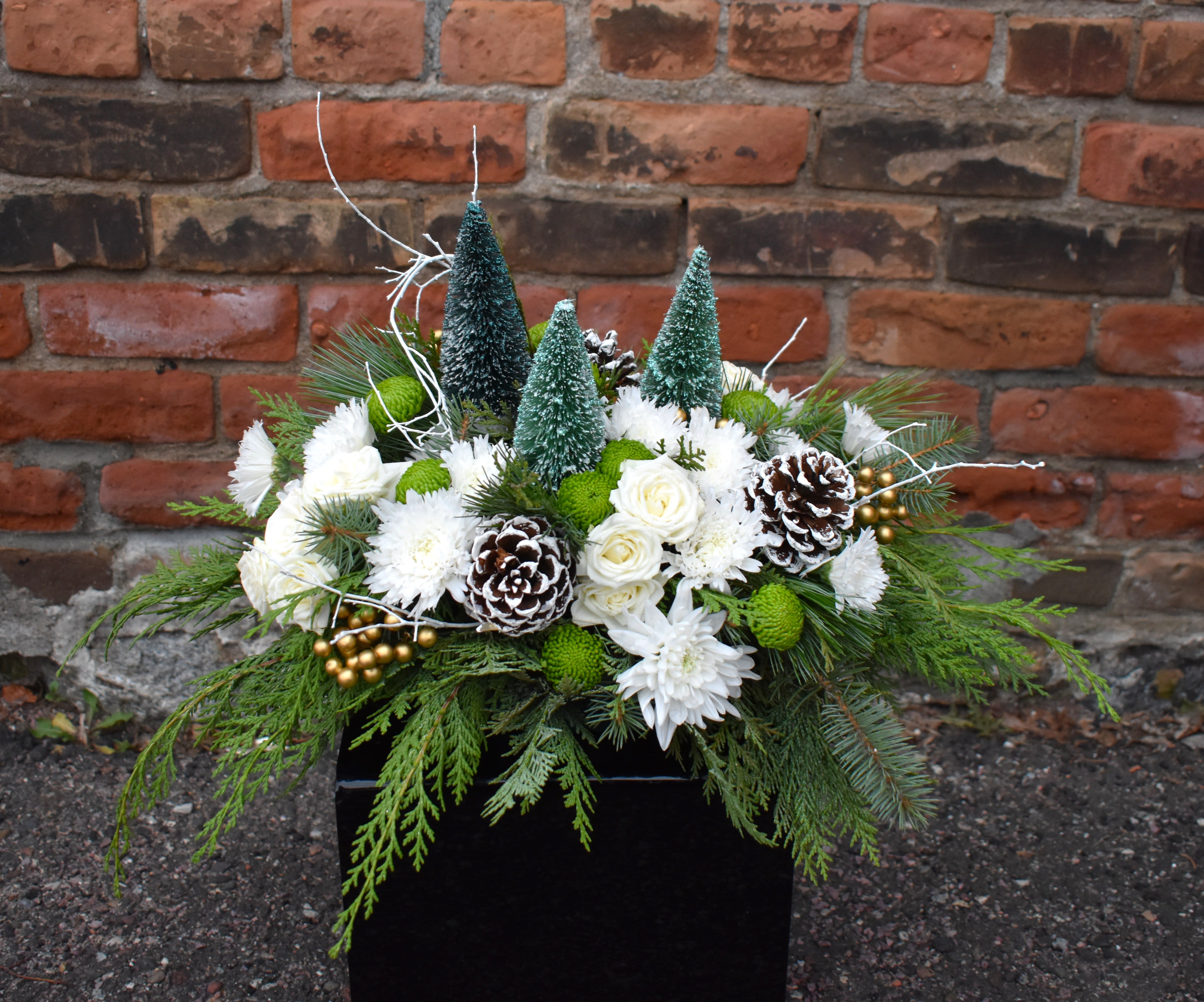 Winter Pine - A design that embodies walking through a peaceful, snow-covered forest! White spray roses, white and green mums, fresh pine, and pinecones are arranged in a low centerpiece and accented by a trio of pine trees, gold berries, and white twiggy branches...a naturally beautiful way to celebrate the season! 