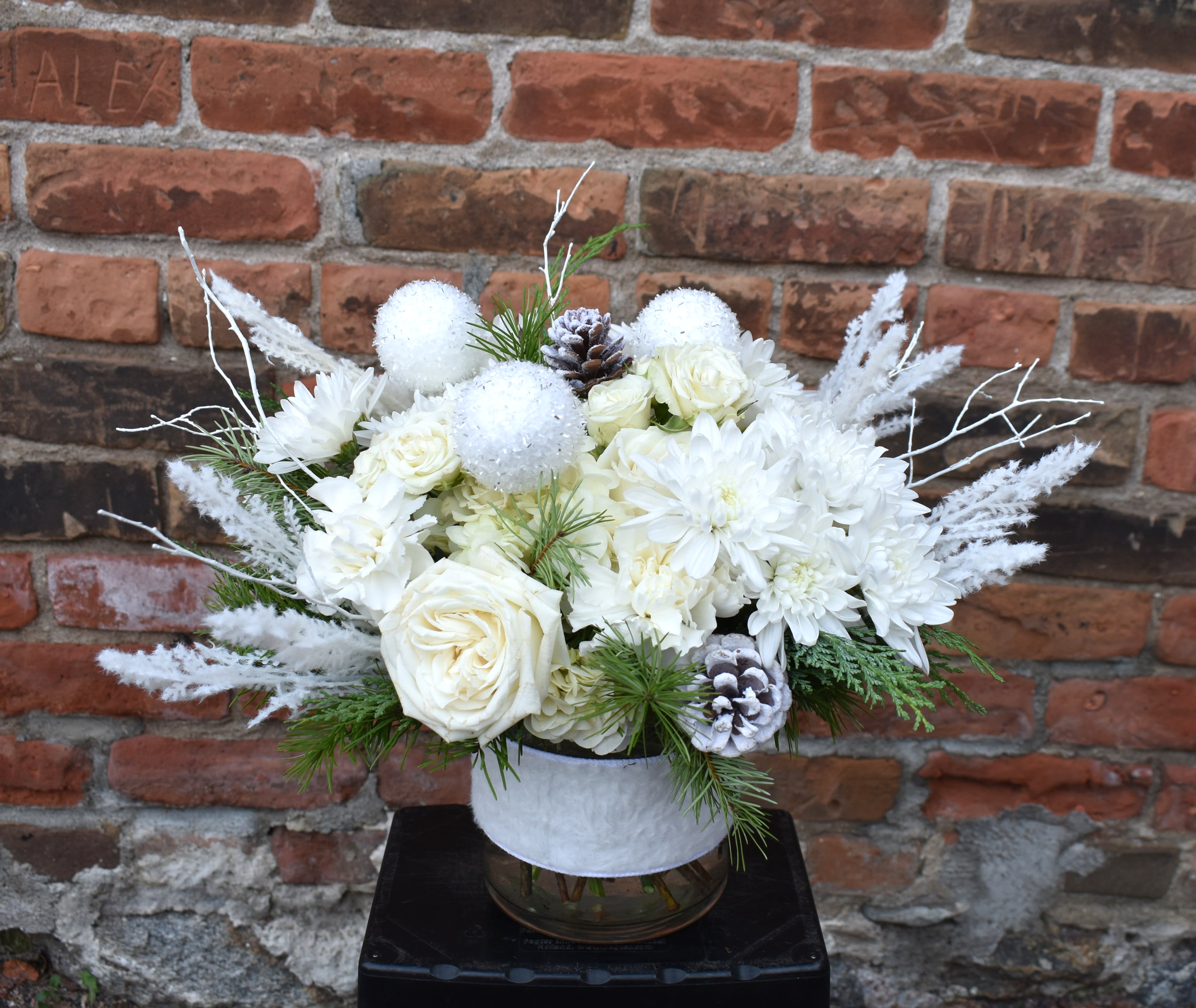 Polar &amp; Plush - A bouquet celebrating the beauty of powdery white snowdrifts, catching snowflakes on your tongue, and cozying up in a warm blanket! White hydrangea, roses, spray roses, mums, and carnations are arranged with fresh pine and accented with white twigs, pinecones, flocked picks, snowballs, and designed in a glass vase with a faux fur ribbon wrap...The perfect way to celebrate living in a polar climate without having to go out in the cold! 