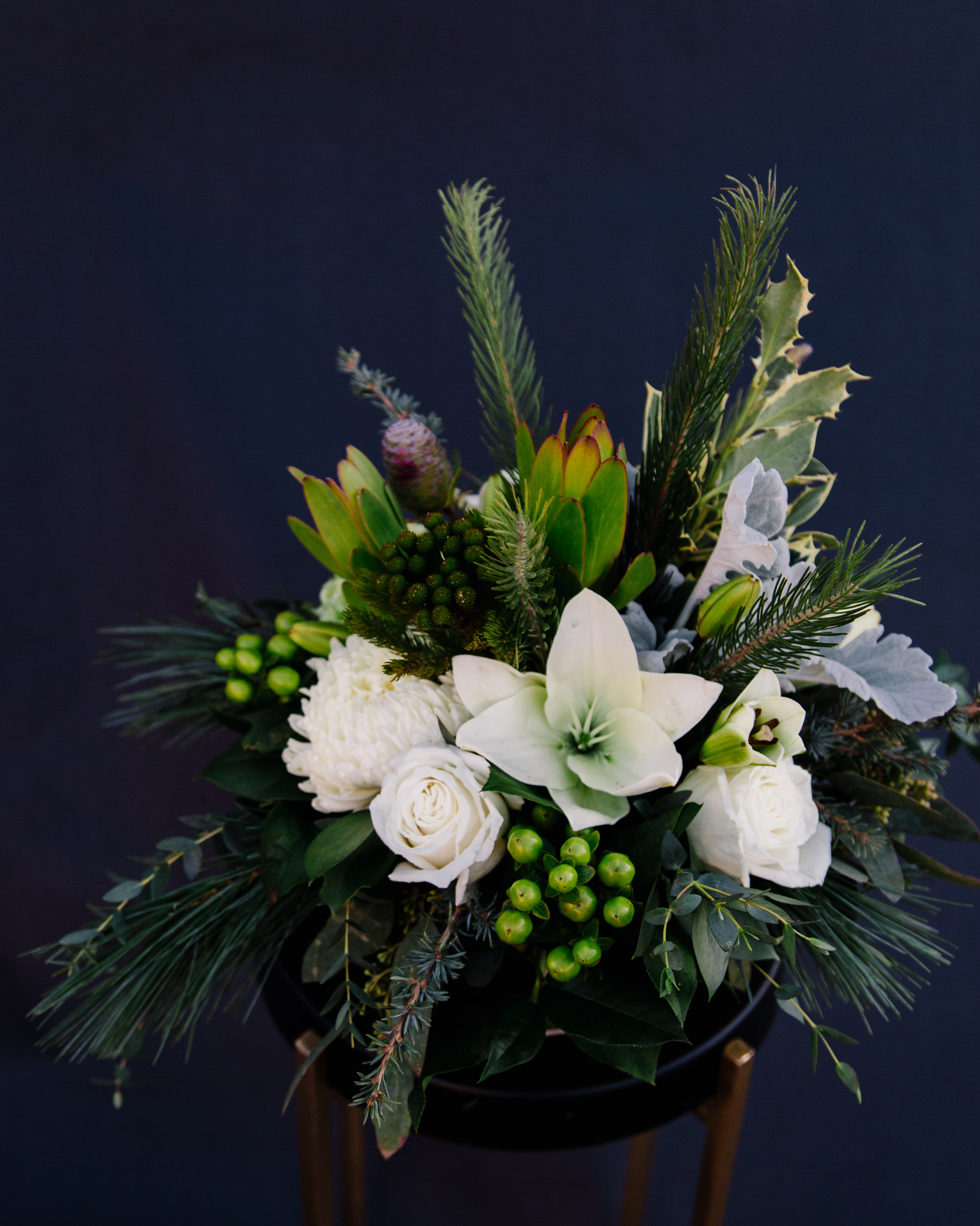 Winter Blooms - This wintery arrangement will make anyone shiver with delight.  This frosty assortment of white and green blooms includes lilies, mums, roses, leucodendron and fresh holly - perfect for that holiday greeting!