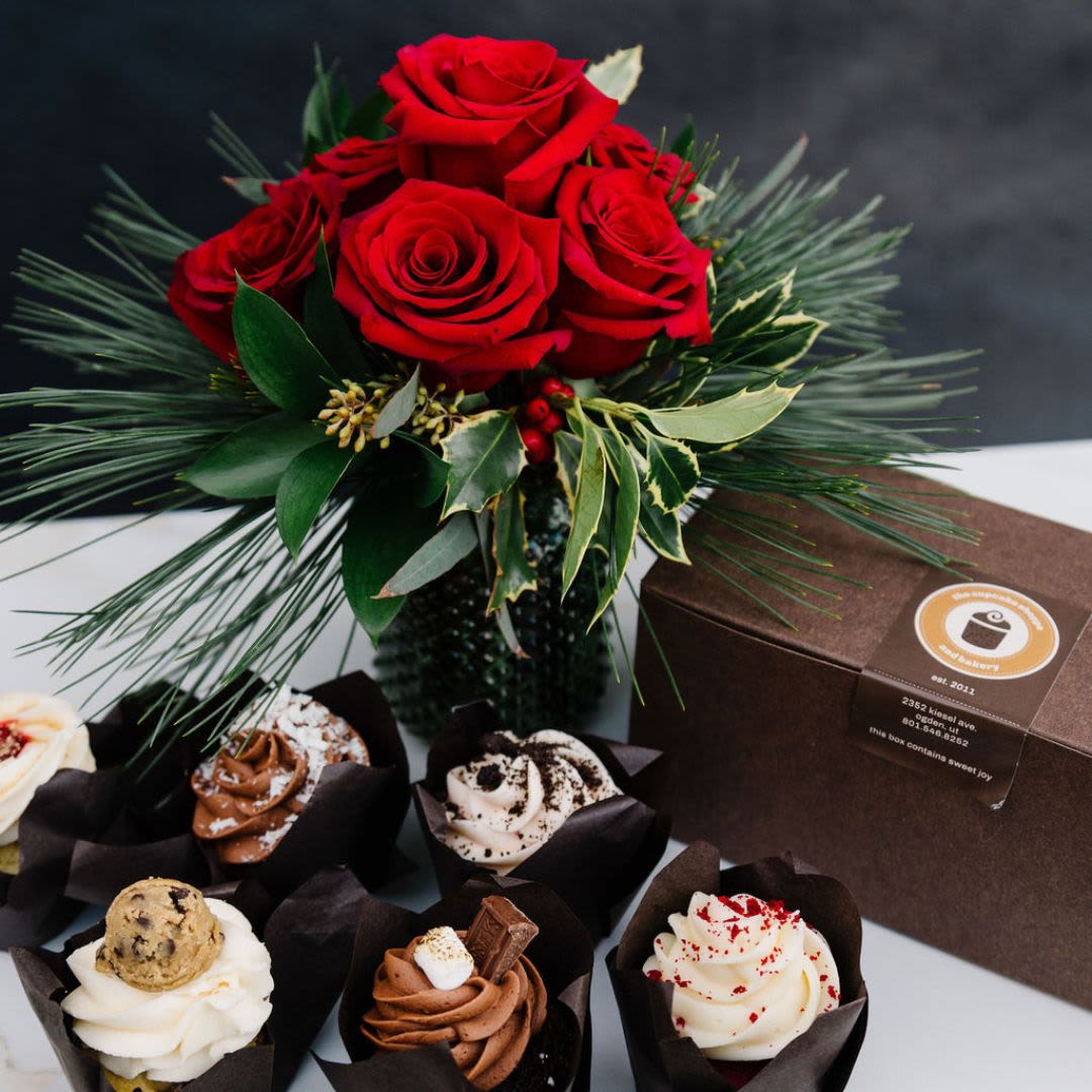 Sweet Holiday Bloom - A delightful pairing of festive cheer and sweet indulgence! This combo features a stunning Christmas floral arrangement adorned with vibrant red roses, pine sprigs, and holly, presented alongside six gourmet cupcakes in decadent flavors. Perfect for gifting or celebrating, this duo combines the beauty of the season with the joy of a delicious treat.