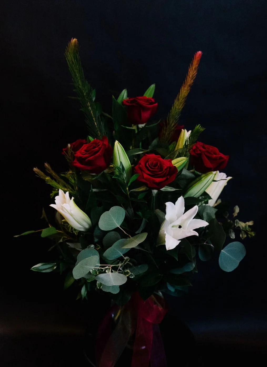 Holiday Love - An elegant winter arrangement of fragrant white lilies and 6 red roses accented with winter pines and eucalyptus.