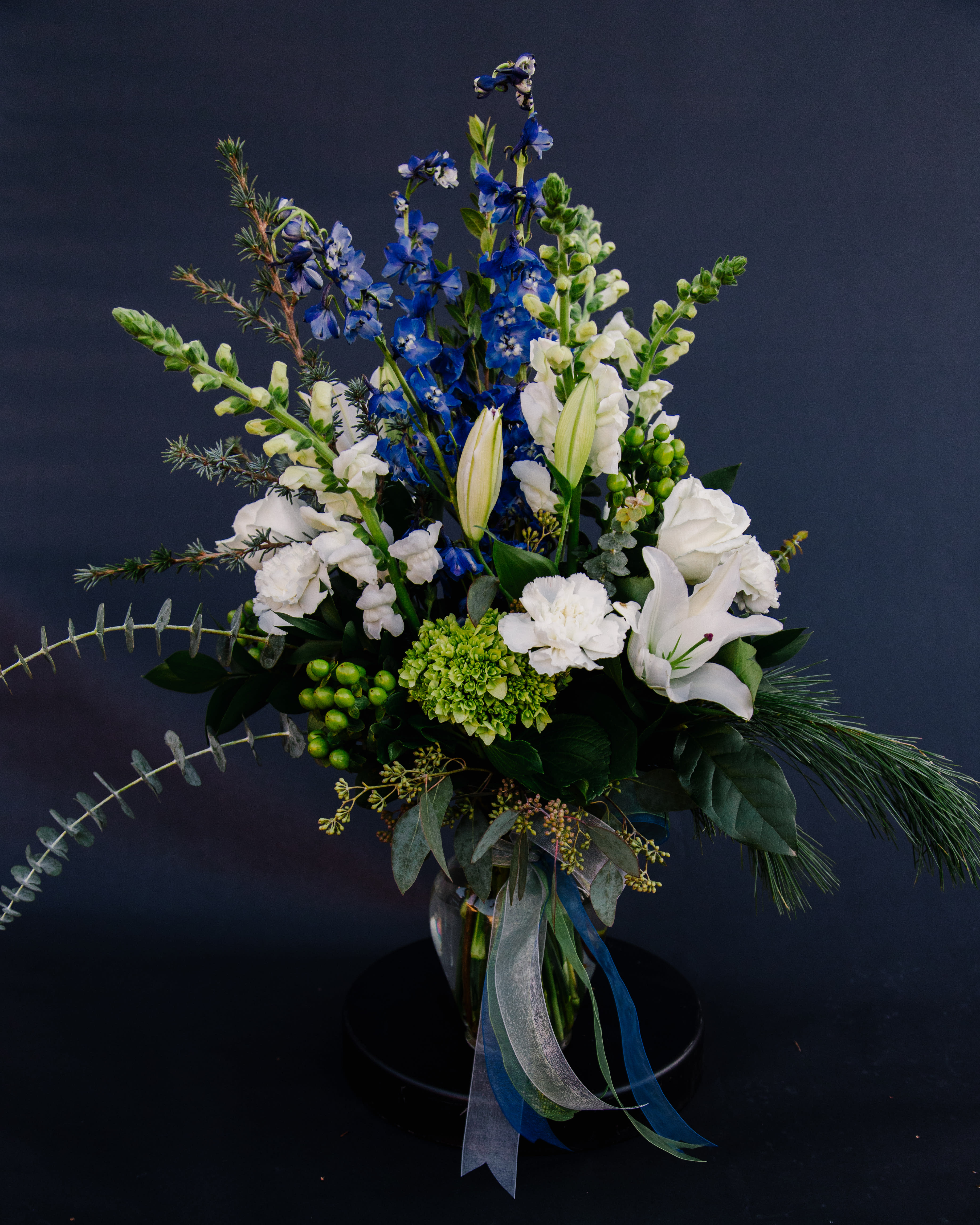 Blue Christmas - This tall winter arrangement includes beautiful blue delphinium and assorted winter white flowers - snapdragons, oriental lilies, &amp; roses.