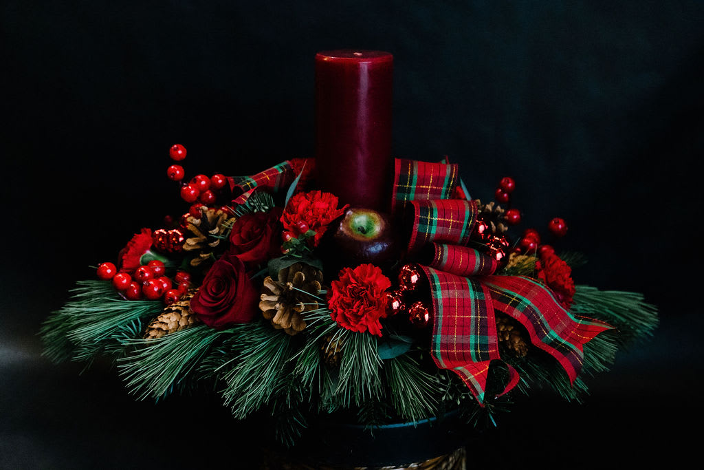 Celebration Centerpiece - A classic holiday centerpiece with winter pines, berries, cones, red carnations and roses with a 9&quot; pillar candle.