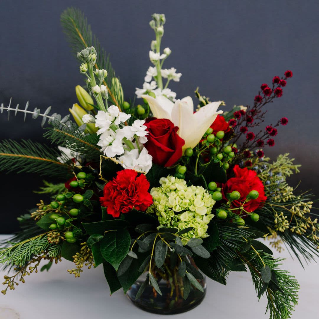 Crimson Snowfall - A timeless, festive arrangement that perfectly captures the spirit of Christmas with its blend of vibrant reds, soft whites and holiday green.  The lush pine provides a subtle, crisp fragrance, evoking the fresh, cool air of a snowy Christmas morning.