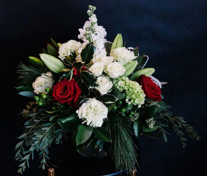 Holiday Kissed - A modern glass cylinder filled with mixed holiday pines; red, white and green flowers accented with a touch of fresh holly.