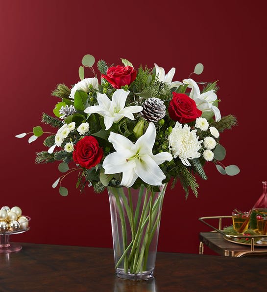 Garden of Grandeur Holiday - Colors of Christmas are on display in our grand holiday arrangement red &amp; white blooms, lush greenery and glistening, snow-tipped pinecones, it’s the perfect gift for celebrating the season in luxurious style. All-around arrangement with red roses; white Oriental lilies, football mums and button poms; accented with green hypericum berries, assorted Christmas greenery and glittery, snowy pinecones