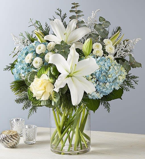 Winter Enchantment Bouquet - All-around arrangement with white kale, button poms, and Oriental lilies; blue hydrangea; solidago painted white and decorated with glitter; accented with spiral eucalyptus and assorted Christmas greenery