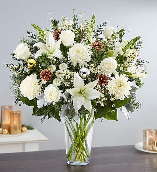 Winter Wonderland Flower Arrangement - it’s filled with white blooms like lilies, roses, mums snapdragons and  shimmering ornaments and pine cone accents to play up its natural beauty
