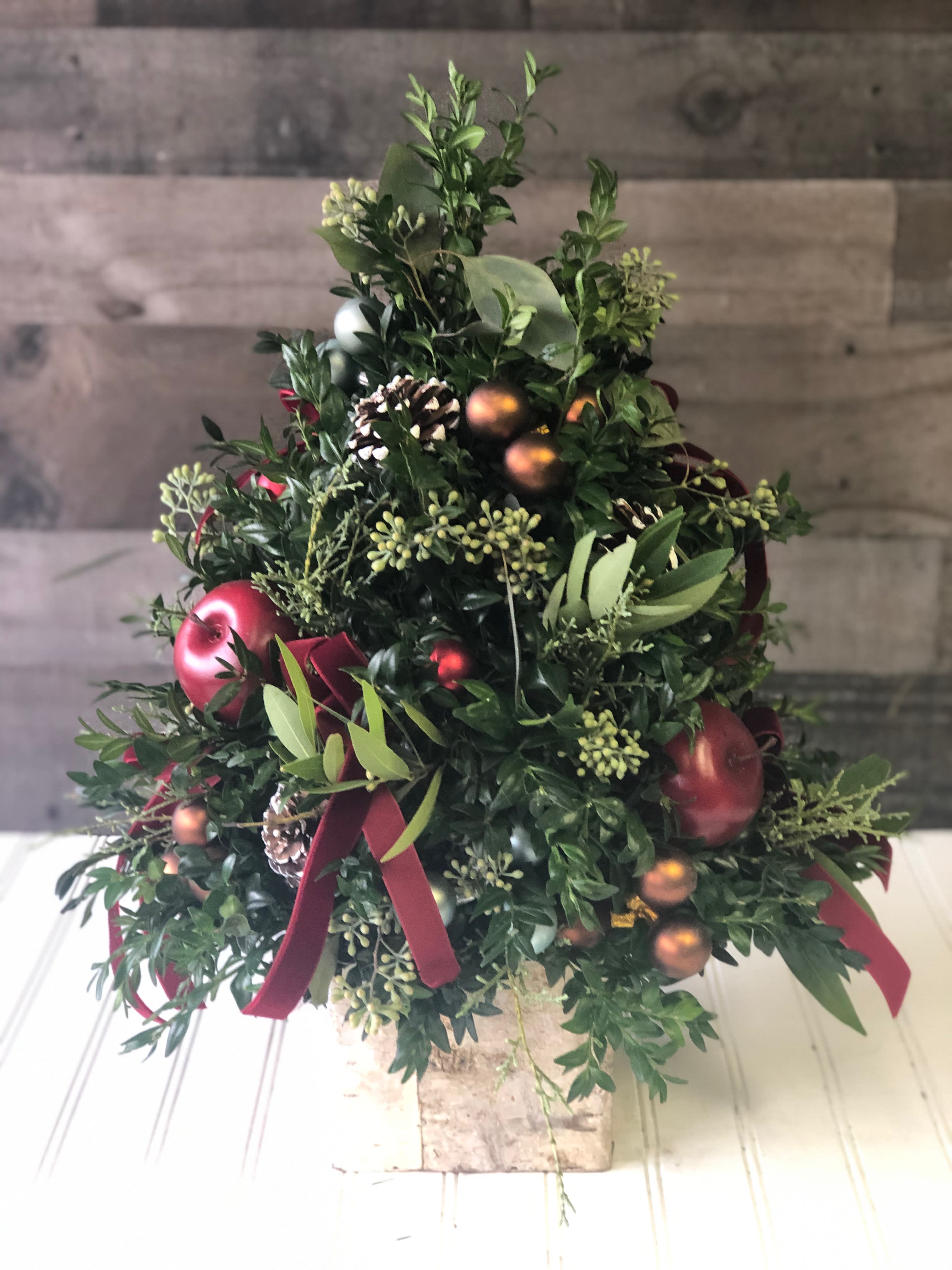 Rustic Holiday Tree - Looking for a rustic Christmas gift? Our Rustic Holiday Tree is the perfect thing to send. Designed in a birch cube with boxwood, eucalyptus, bay leaf, winter greens, faux apples, shimmer orbs and accented with velvet ribbons.