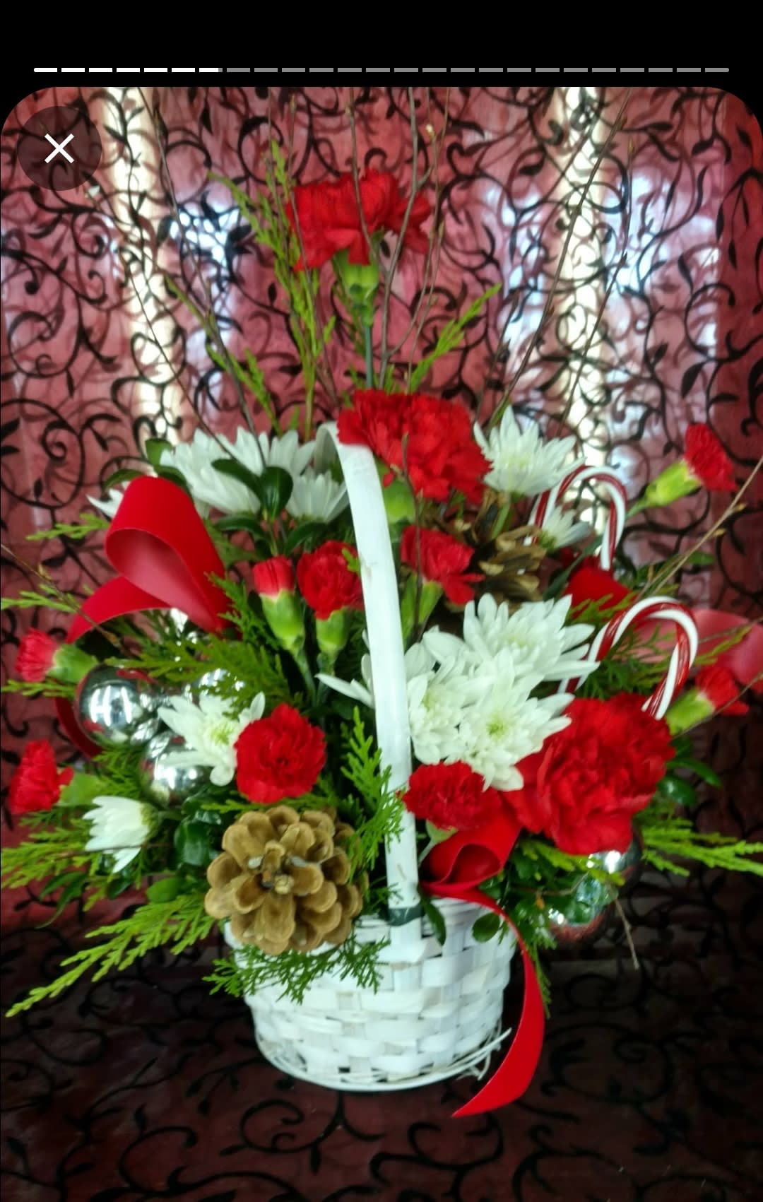 Santa's Secret - This white basket is filled with reds and whites in a variety of flowers and textures such as carnations, cushion poms, velvet ribbon and candy canes. 