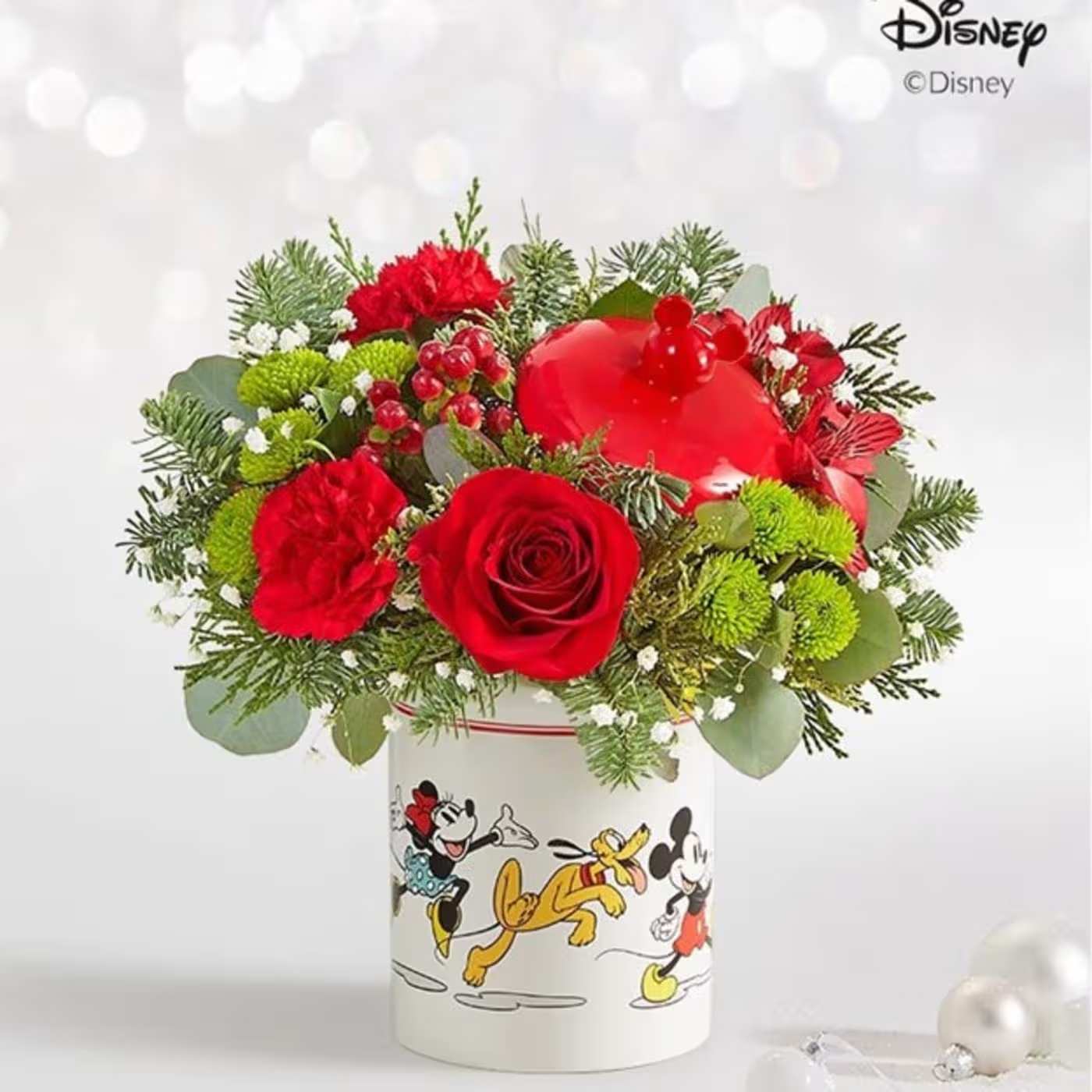 Disney Micky Mouse &amp; Friends Holiday Cookie Jar - Share a gift full of character(s)! Part of our Disney collection, our handcrafted winter-fresh bouquet is designed in our whimsical Mickey Mouse and Friends cookie jar. Featuring iconic images, the food-safe jar can be used to store treats and a multitude of other items long after the flowers are gone. All-around arrangement of red roses, carnations, and mini carnations, and white Peruvian lilies (alstroemerias) and cushion poms, accented with baby’s breath, assorted winter greenery, and green metallic ball ornaments