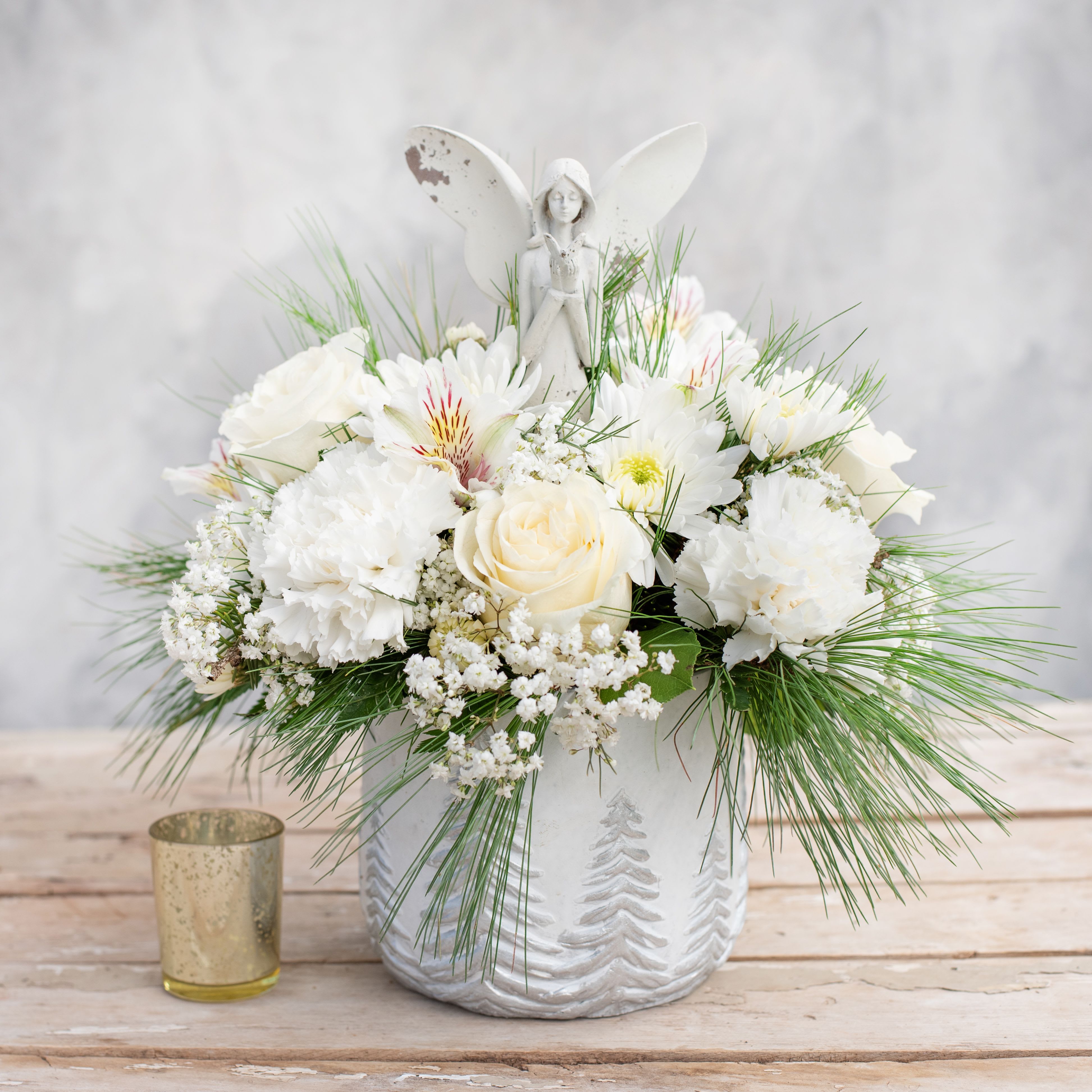 Angel - Imagine this divine arrangement on your kitchen table for the Holidays.  There's a 12&quot; rustic guardian angel emerging from a white ceramic cylinder embossed with evergreen trees and the angel is surrounded by a white cloud of roses, carnations, mums, alstroemeria, baby's breath and accented with evergreens.  