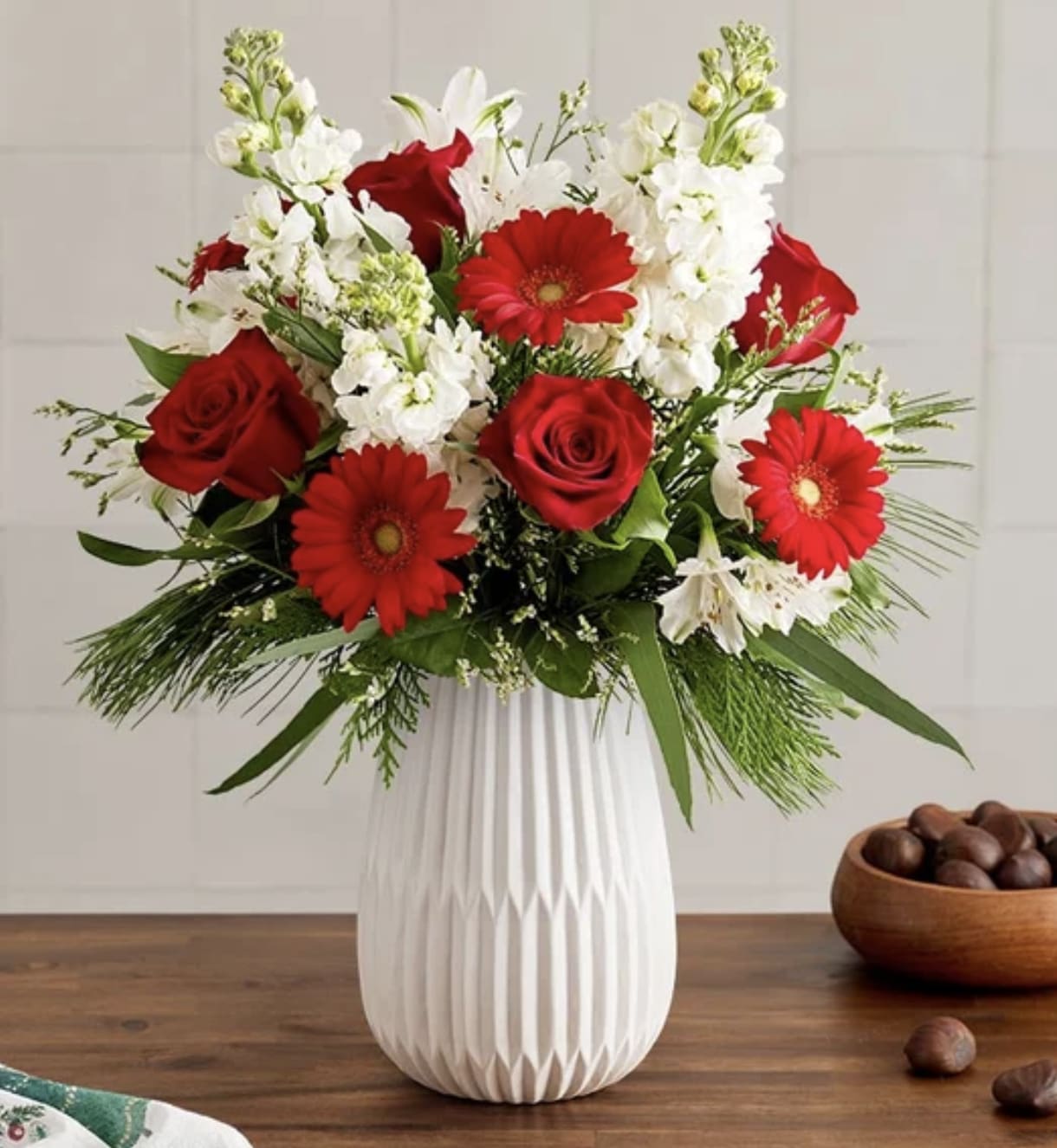 Dazzling Christmas Bouquet - Celebrate the most magical time of year with our dazzling bouquet. A rich gathering of blooms in classic red and white is accented by lush greenery. Hand-designed in our keepsake White Modern Vase, featuring a tapered design and matte finish, it’s a gift that brings the joy of Christmas to family and friends, near and far.  All-around arrangement with red roses and mini Gerbera daisies, white stock, Peruvian lilies (alstroemeria) and Limonium; accented with feather willow eucalyptus and assorted Christmas greenery Artistically designed in our Modern White Vase, with a tapered design and a matte finish, for a contemporary look that also has a softness to it, to complement everyday arrangements.  To ensure lasting beauty, Peruvian lilies may arrive in bud form and will fully bloom over the next few days.