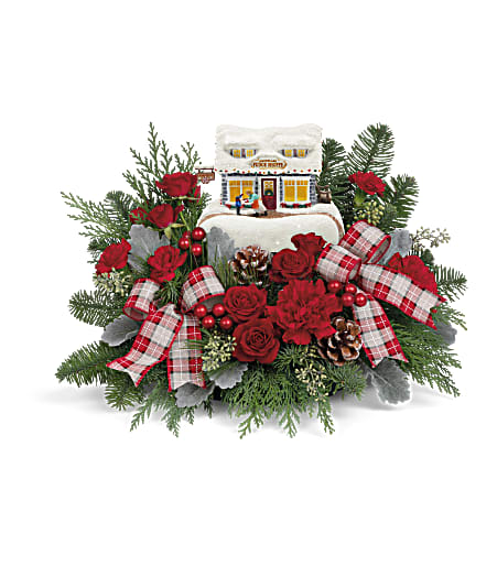 TF Thomas Kinkade Sweet Shoppe Bouquet 2022 - A sweet treat they'll adore for many Christmases to come! Nestled in roses and winter greens, this treasured collectible glows from within in classic Thomas Kinkade style.  Red spray roses, red carnations and miniature red carnations are arranged with noble fir, cedar, white pine, seeded eucalyptus and dusty miller. Delivered with Teleflora's Thomas Kinkade's Sweet Shoppe Keepsake. Approximately 17&quot; W x 11 1/4&quot; H
