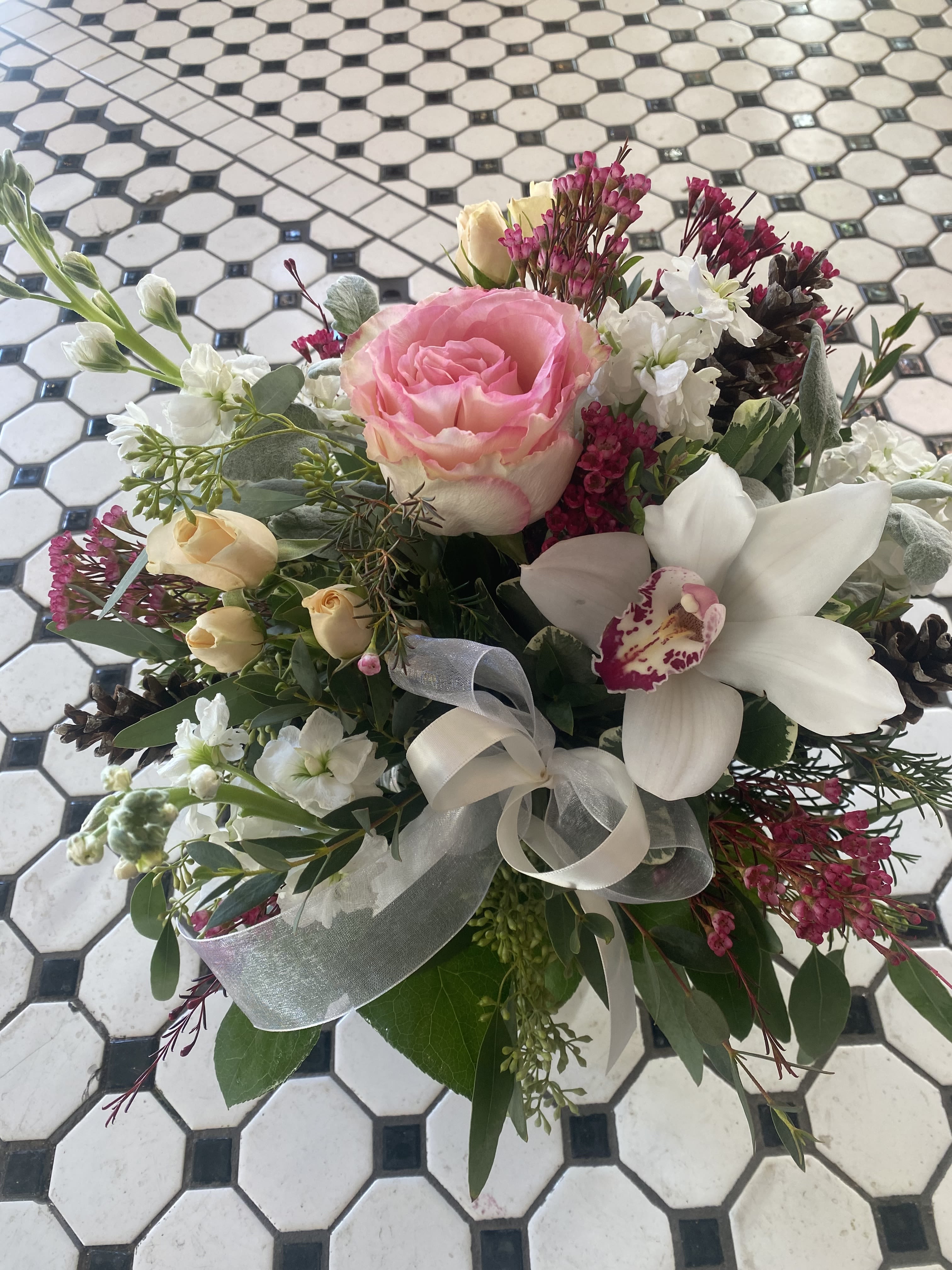 Holiday Stardust - &quot;Holiday Stardust&quot; will add a sprinkle of magic to anyone's holiday. With soft colors of pinks and whites, this arrangement features a high end garden Rose, Cymbidium Orchid, Stock and Pinecones. It is the perfect arrangement to add a touch of elegance to any space!