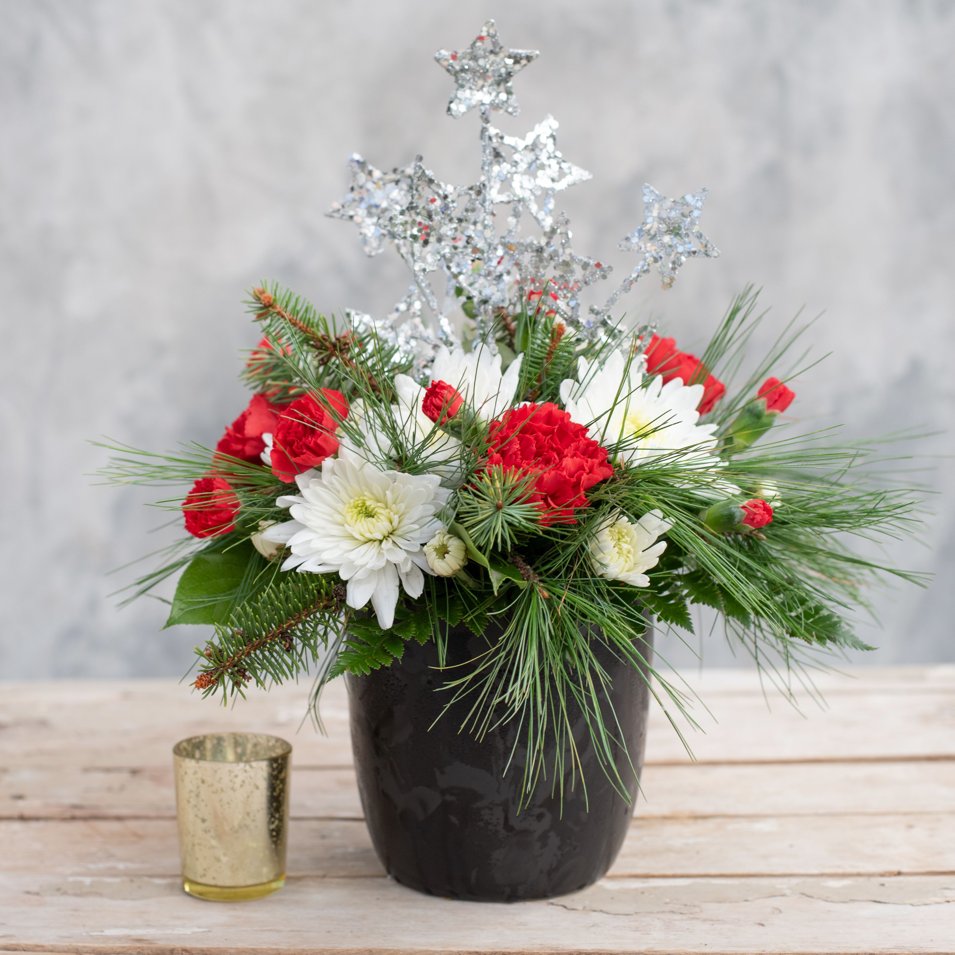 Holiday Stars - Perfect as a Holiday hostess gift or for your own entertaining.  This 5&quot; black matte ceramic cylinder is bursting with red carnations, white mums, red mini-carnations and evergreens and topped with a keepsake sparkly star pick.   