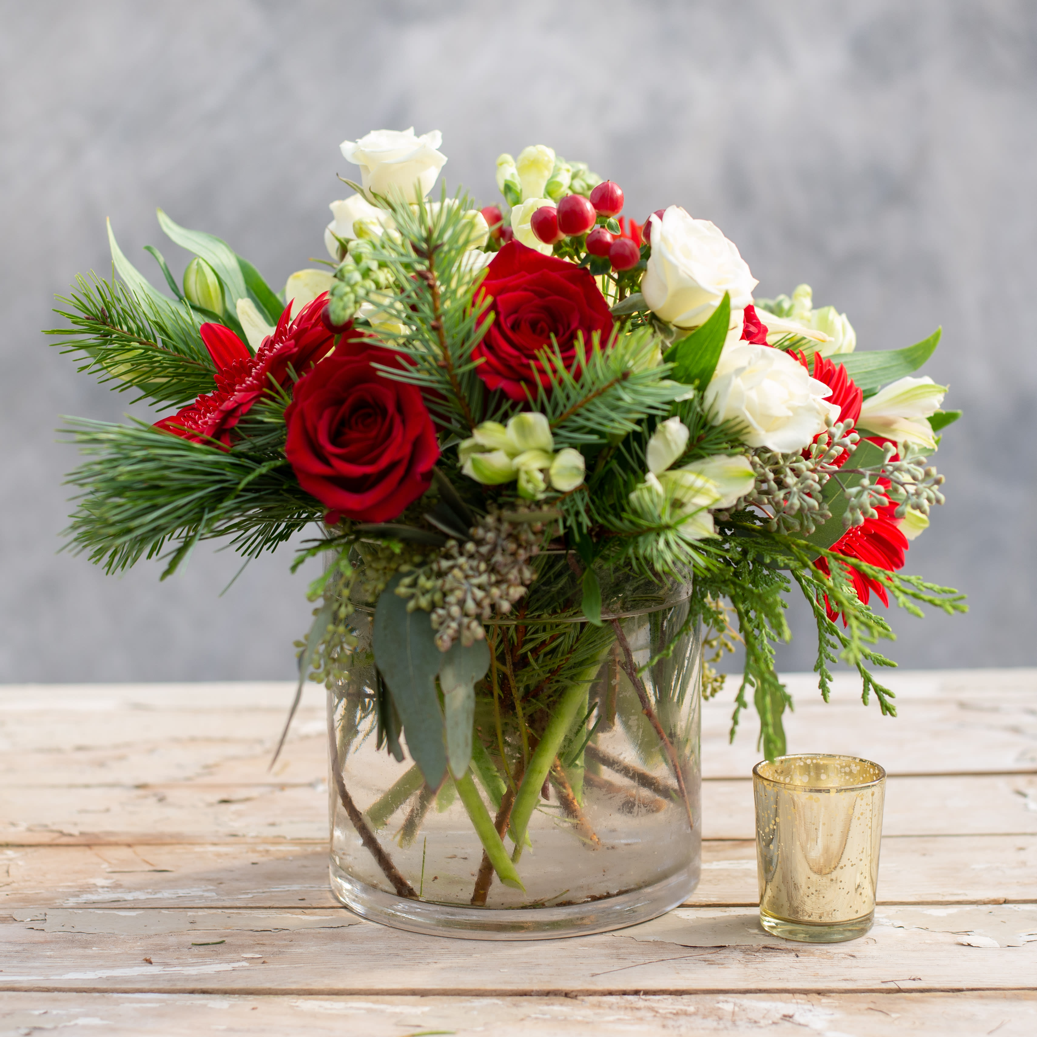 Joy - This elegant arrangement is the perfect centerpiece for any holiday table.  The 6&quot; x 6&quot; glass cylinder is full of red and white premium flowers, including Lilies, roses, gerbera daisies and snap dragons.  Accented with hypericum berries, seeded eucalyptus and evergreens.   