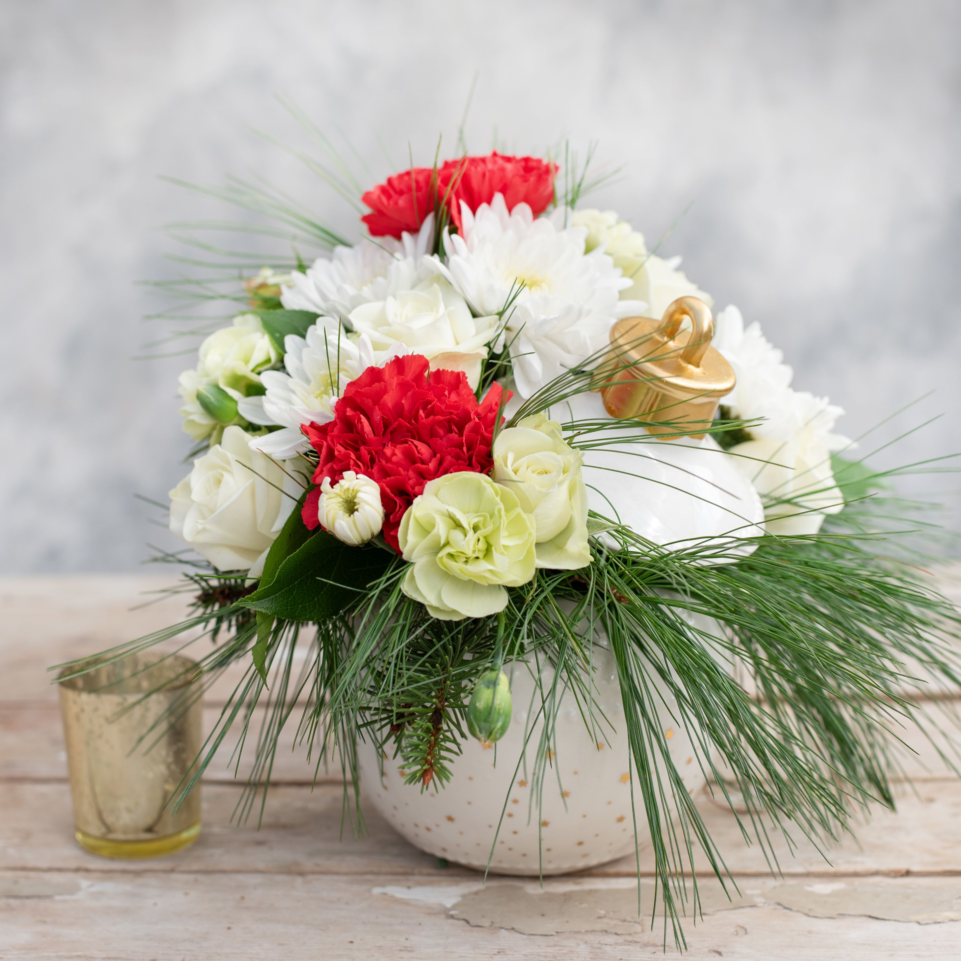 Noel - What better way to celebrate the holidays then with this festive arrangement. A white ceramic ornament with gold stars and a lid filled with red carnations, white mums, white spray roses, green mini-carnations and evergreens.  
