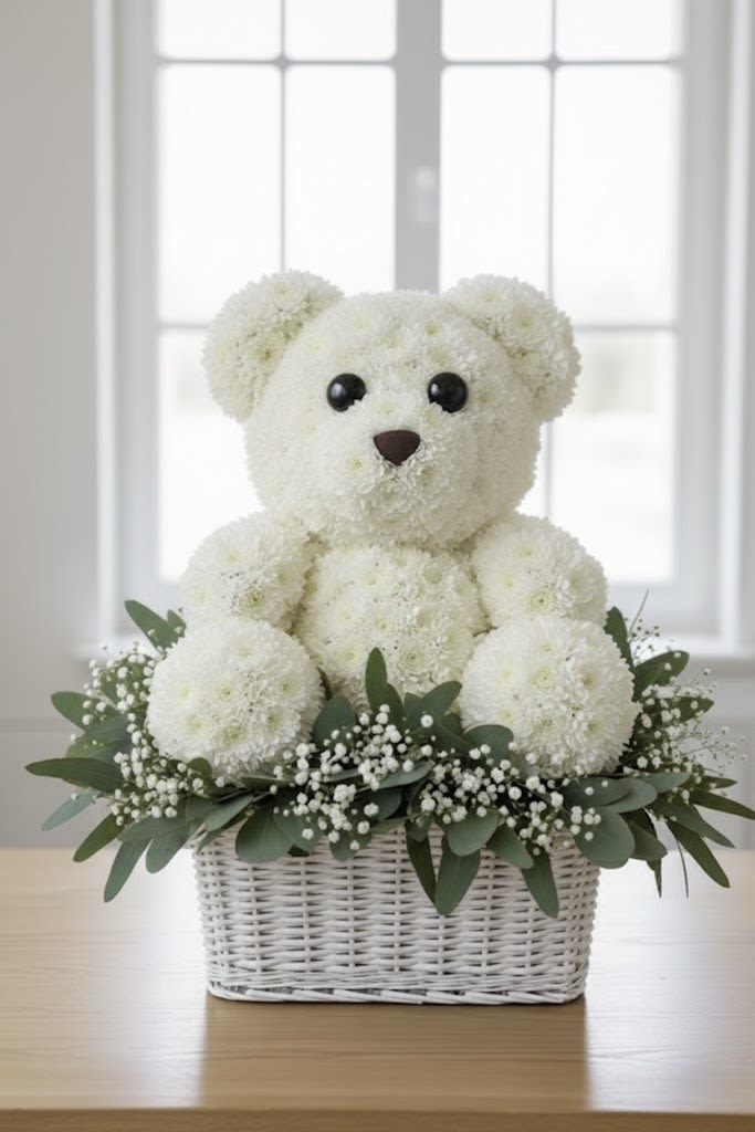 The Cuddle Bear Bloom By Black Cat Florist - A hug made of flowers! This one-of-a-kind, handcrafted bear is created entirely from pristine white flowers, nestled among soft eucalyptus greens and delicate white baby's breath. It is presented in a chic, handle-less neutral basket, and is adorned with an elegant double-layer blue satin bow for a boy or pink bow for a girl. This unique arrangement makes a perfect, sophisticated, and memorable gift for welcoming a new baby boy/girl a christening, or simply expressing enduring love and innocence.