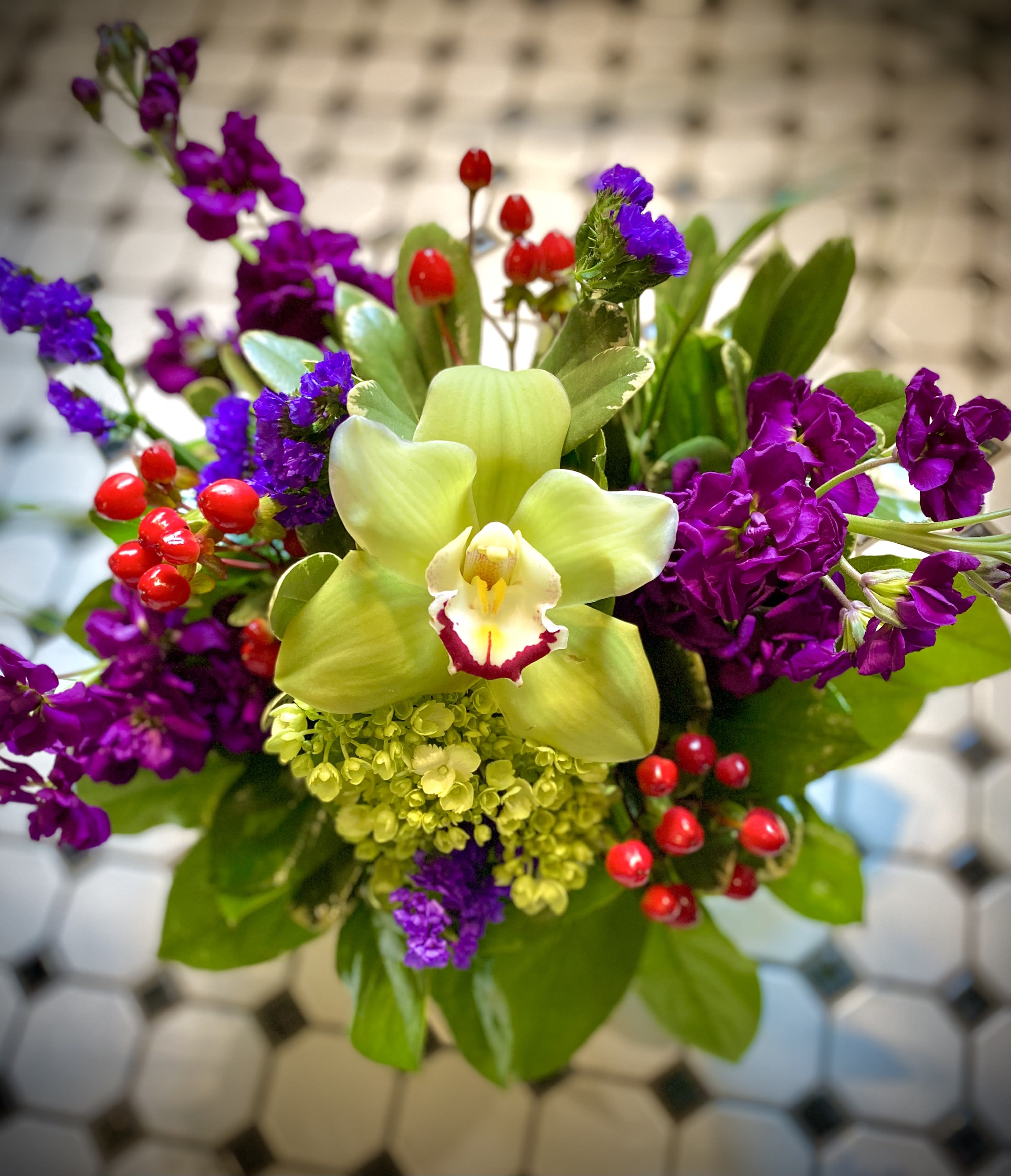 Winter's celebration - Beautiful tones of rich purple, red and green grace this beautiful design celebrating late winter. Includes cymbidium orchid, hypericum berry, green hydrangea, and stock. Perfect for an office or home space