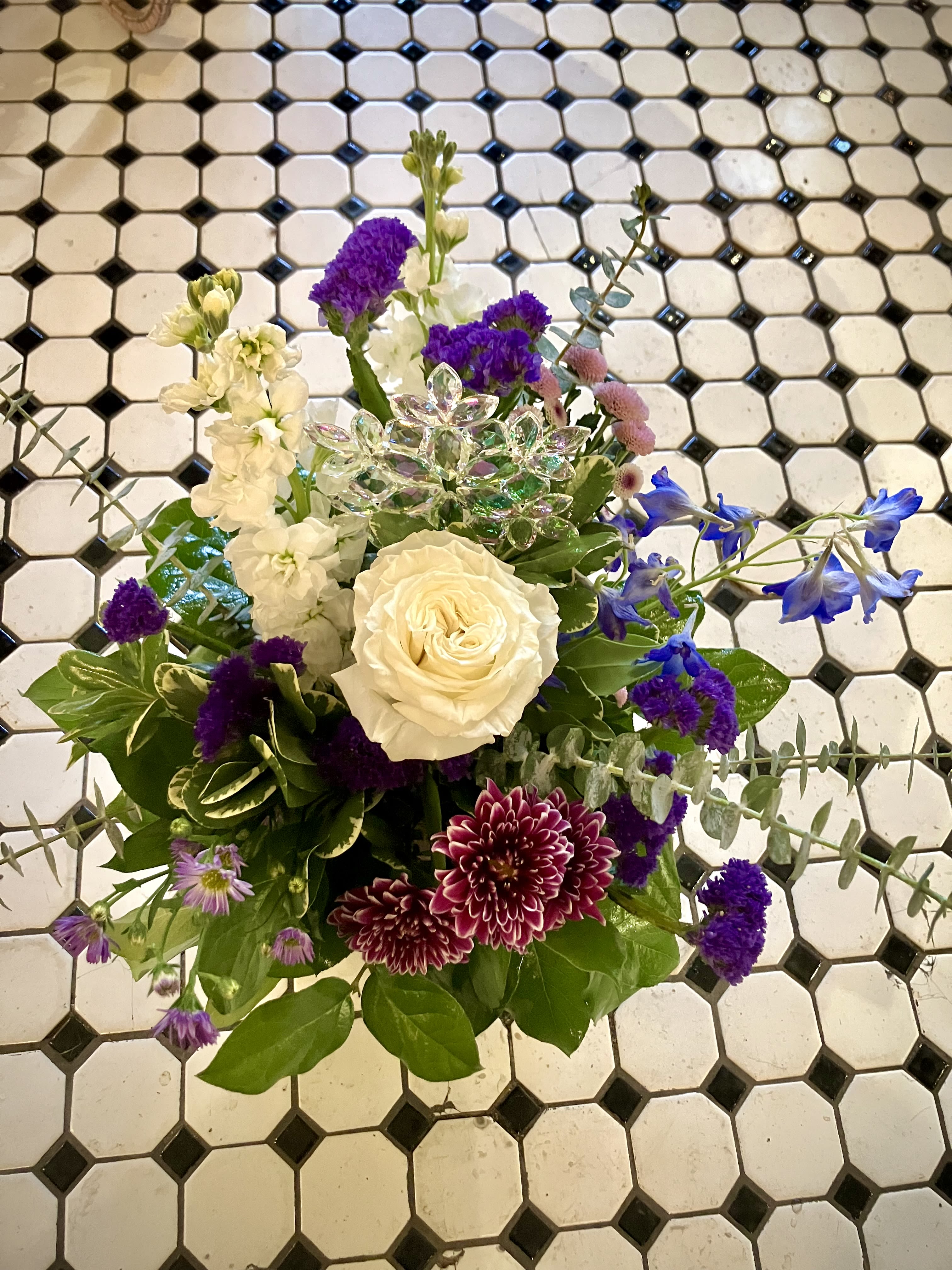 Snowflake Garden - This gorgeous holiday arrangement features a beautiful Rose, Mums, Stock, Status and a keepsake ornament! In colors of Purple, White and Blue, it is the perfect touch to add to anyone's home this winter season. 