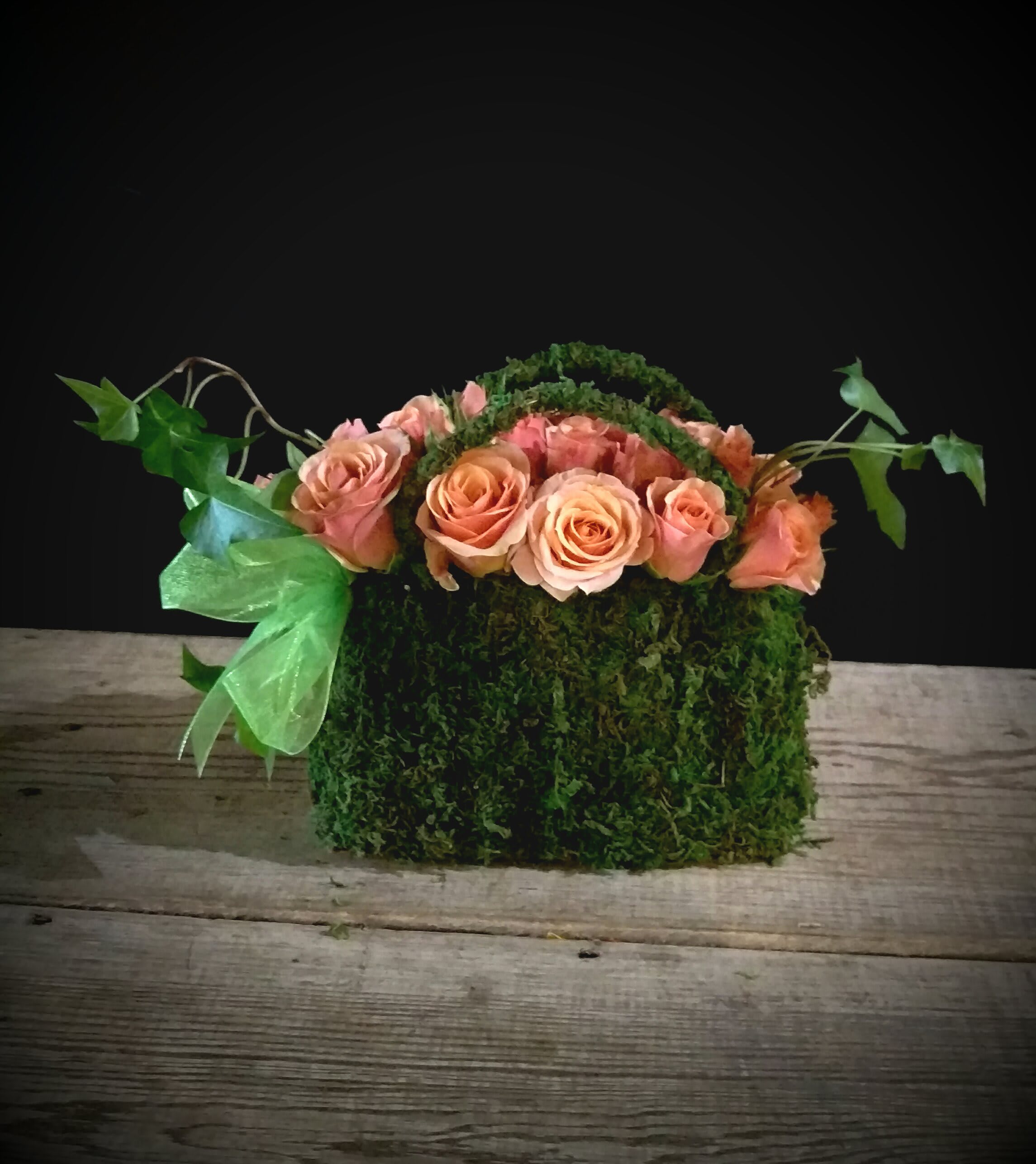 Granny White Moss Purse - Named after a well known street in the South of Nashville.. Granny White features a mossed &quot;purse&quot; tucked overflowing with the sweetest lil peachy pink spray roses and accented with a ribbon.