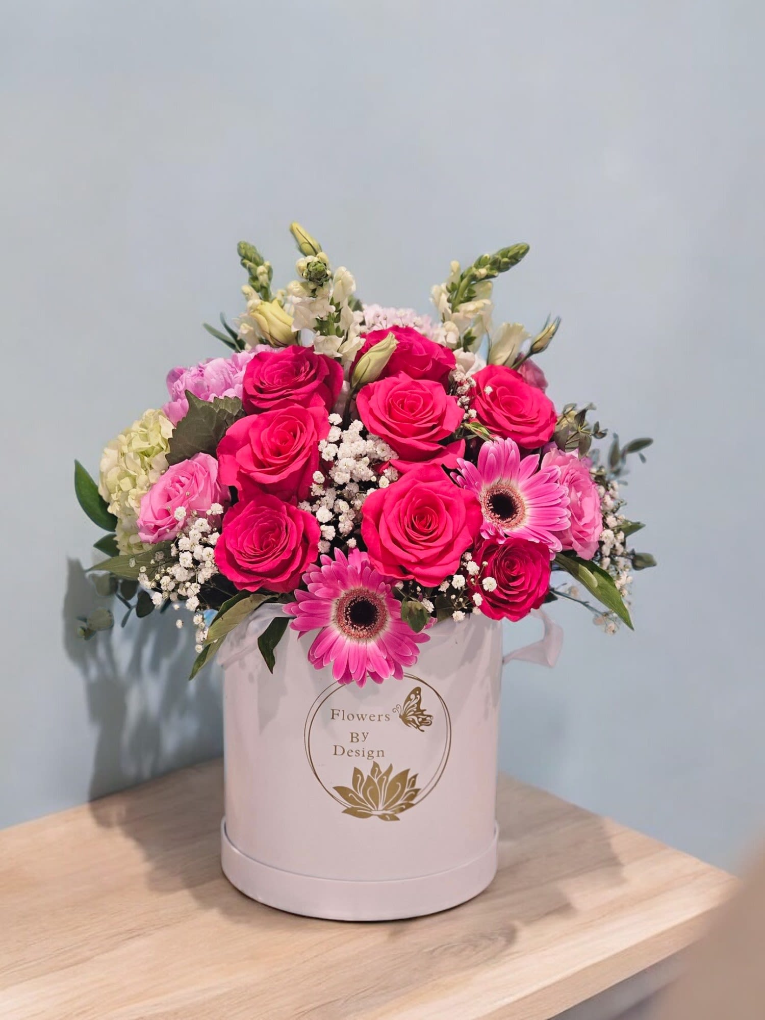 Pink Petal Paradise - It emphasizes the abundance of hot pink roses, gerberas, and peonies against the backdrop of white snapdragons and green lisianthus, all accented with lush greenery and delicate filler. The name captures the luxurious and harmonious blend of pink hues with the freshness of greenery in a pristine white box.