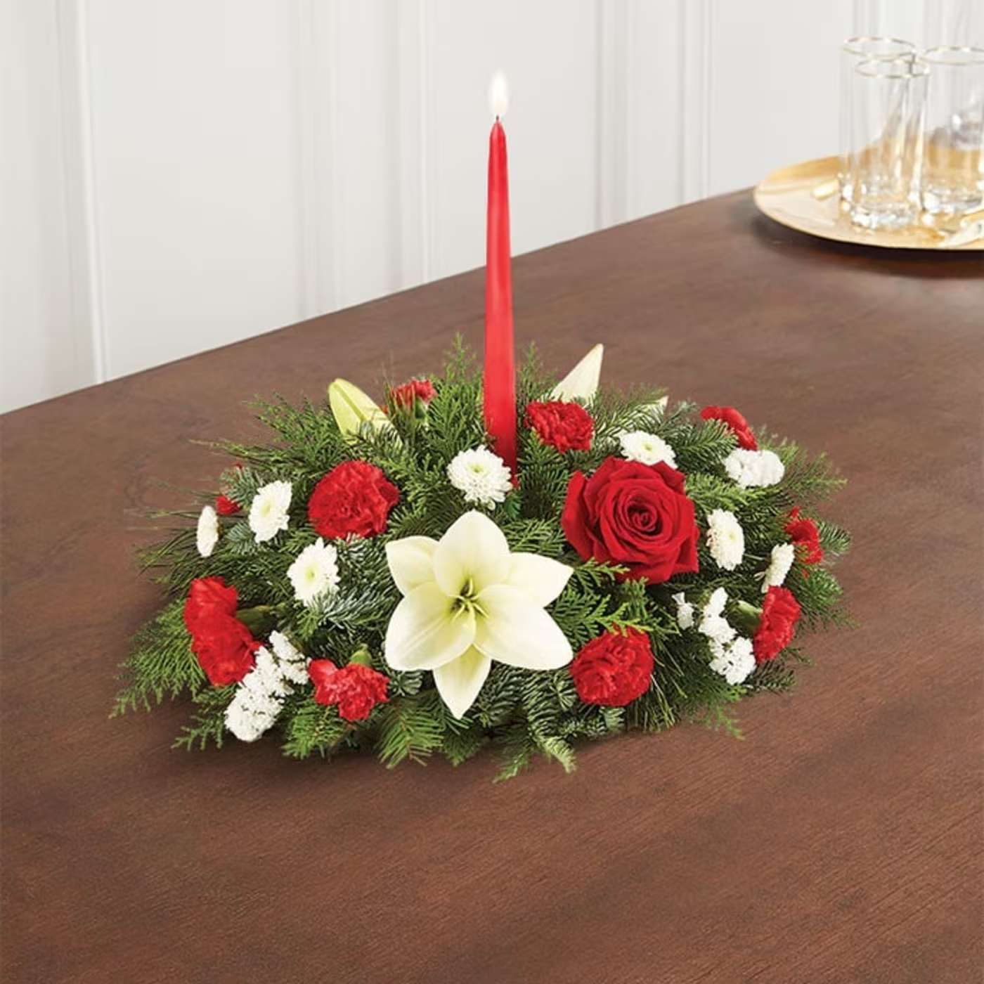 Traditional Christmas Centerpiece - Our classic table arrangement is an idyllic centerpiece for your Christmas celebration. Beautifully designed with long-lasting blooms in seasonal colors, this fragrant gathering features red taper candles to cast a warm, inviting glow throughout the holidays. Centerpiece arrangement with red roses, carnations, and mini carnations, and white Asiatic lilies, button poms, and statices, accented with assorted Christmas greenery